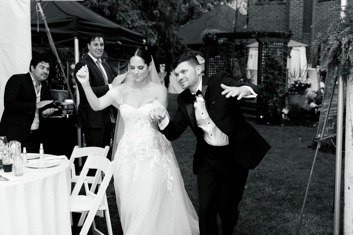 Black and white photo of wedding celebration with guests dancing under outdoor tent.