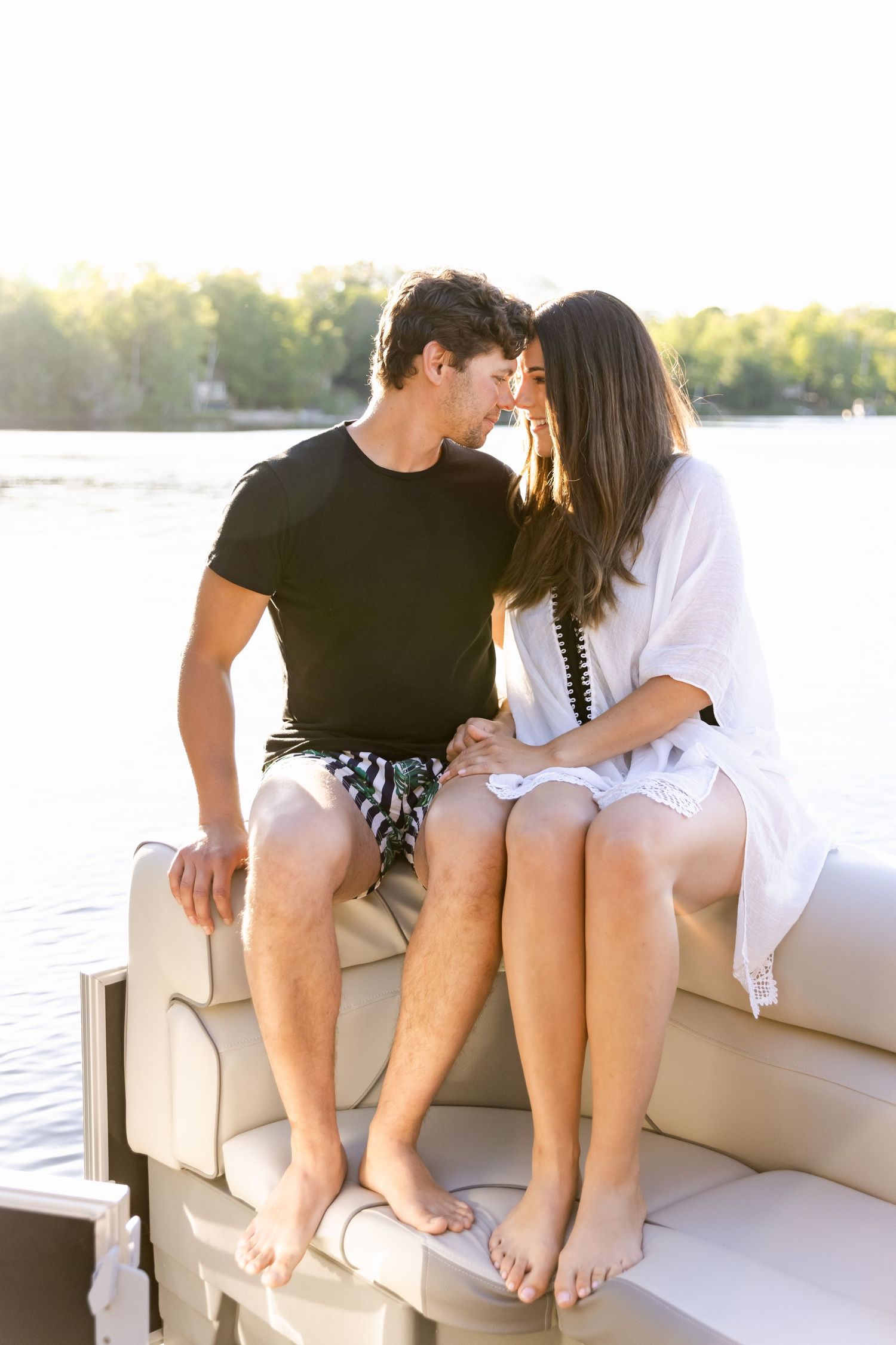 Intimate moment between couple sitting on boat cushions with lake and sunset in background.