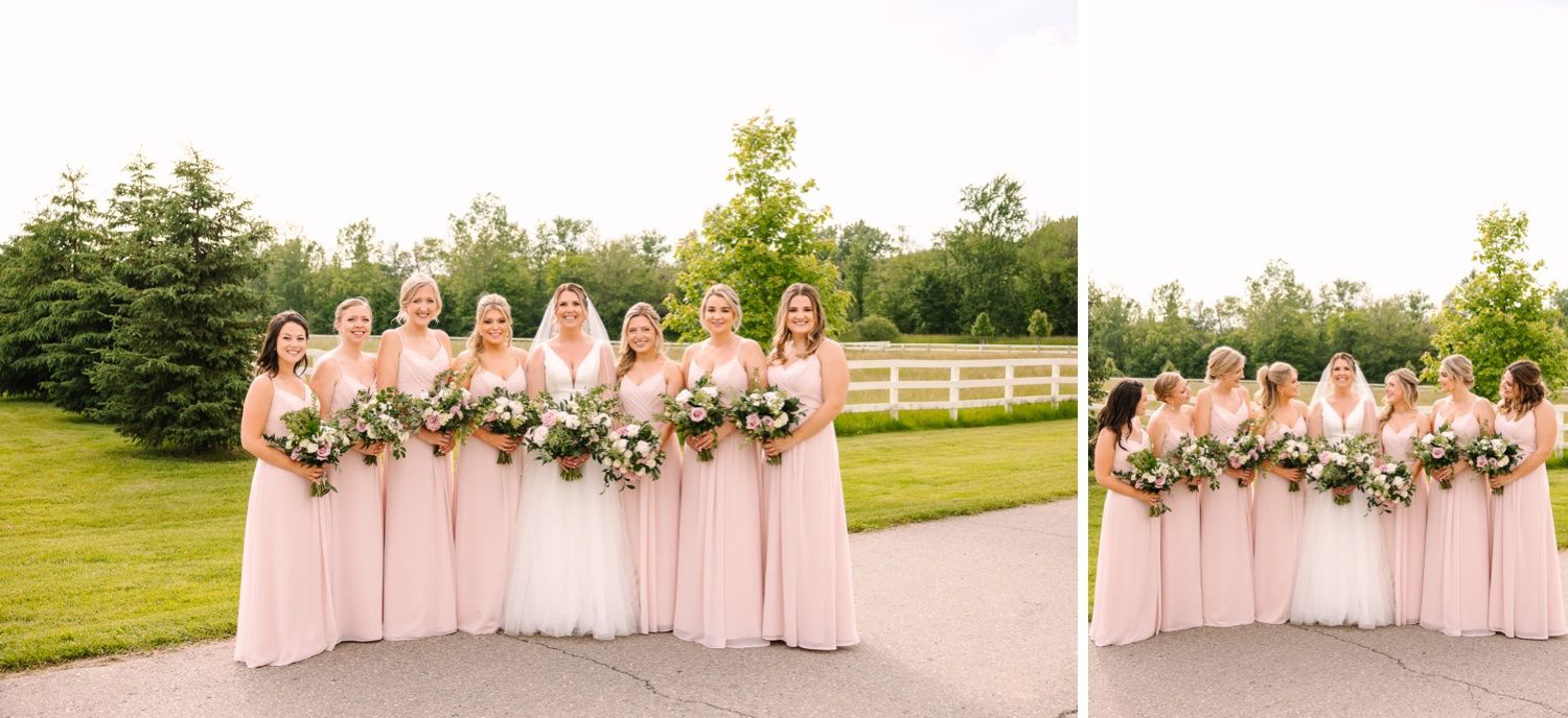 Wedding party in soft pink dresses pose for group photos against a white fence backdrop.