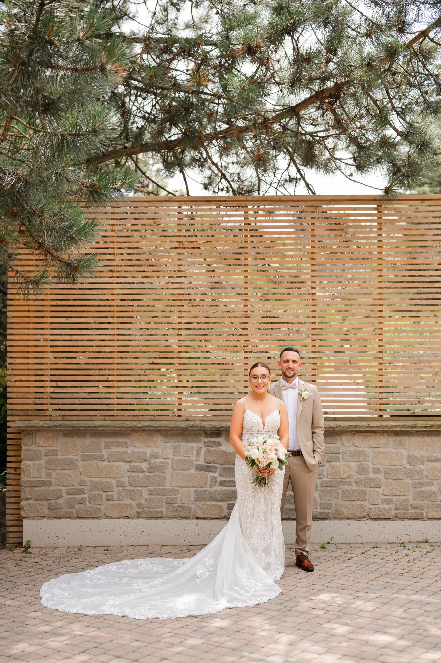 Elegant wedding portrait with pine trees and wooden slat wall backdrop on brick paver patio.