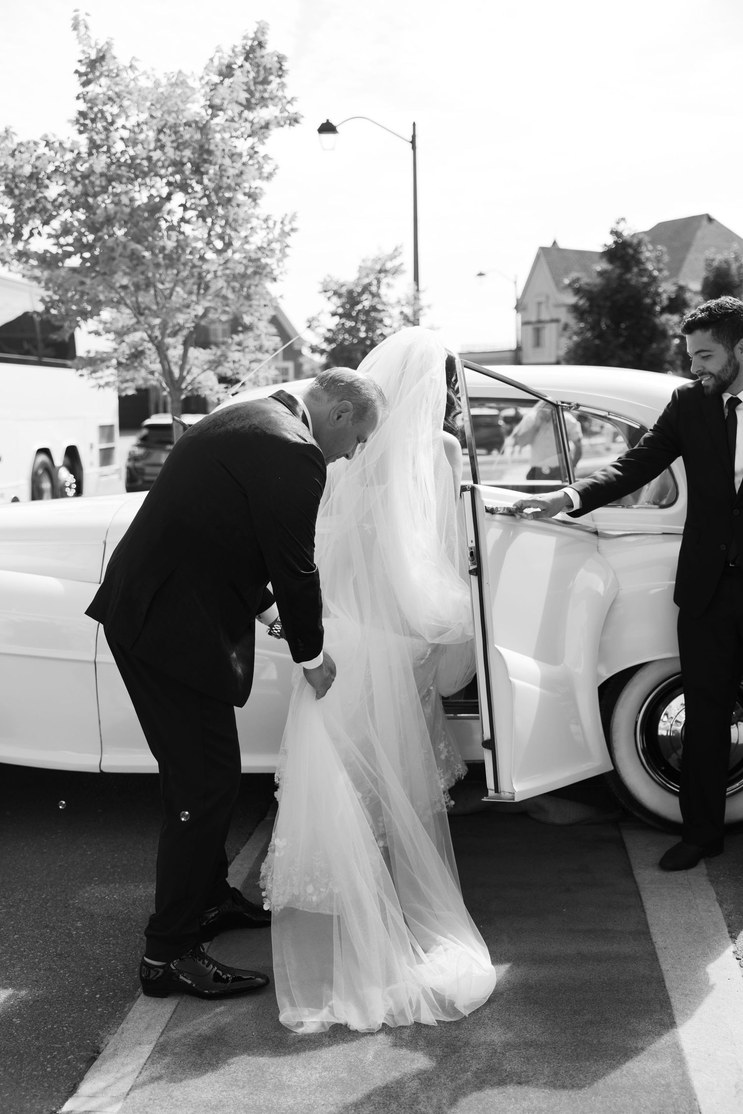 Helping the bride into a classic white wedding car on her special day.