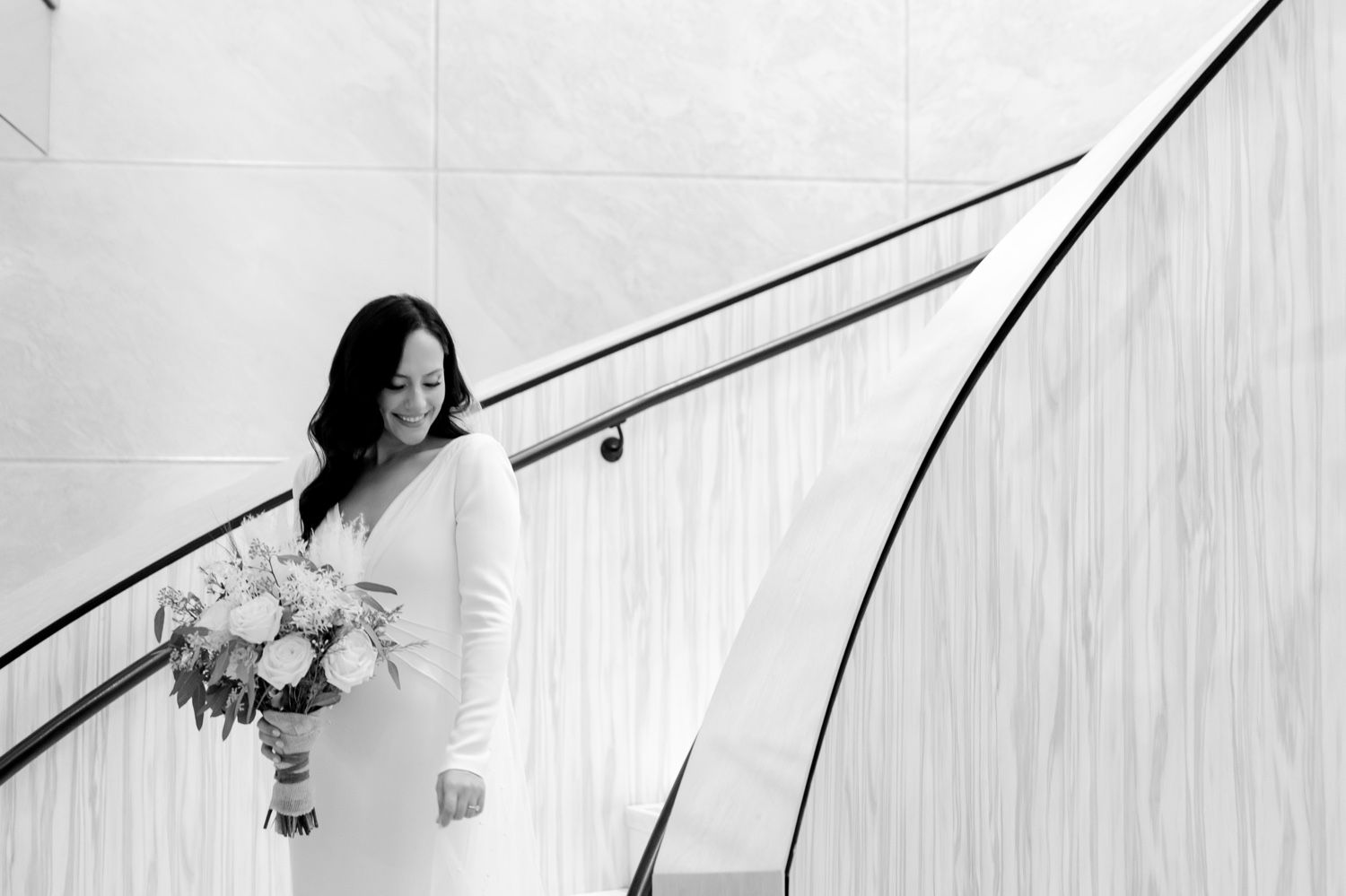 Black and white wedding portrait showing bride with bouquet on curved staircase.