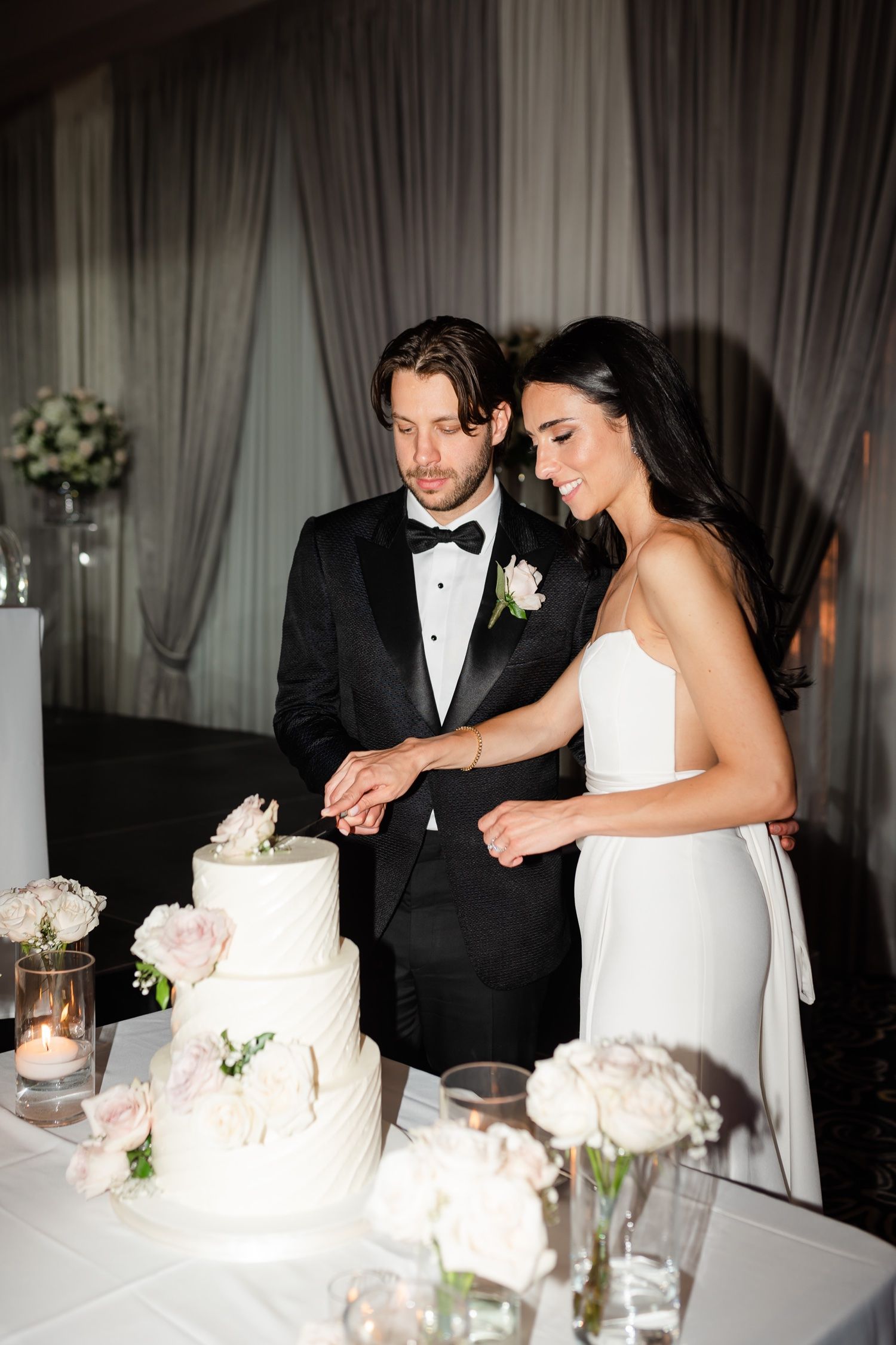 Intimate cake cutting moment at elegant reception with white floral decorations.