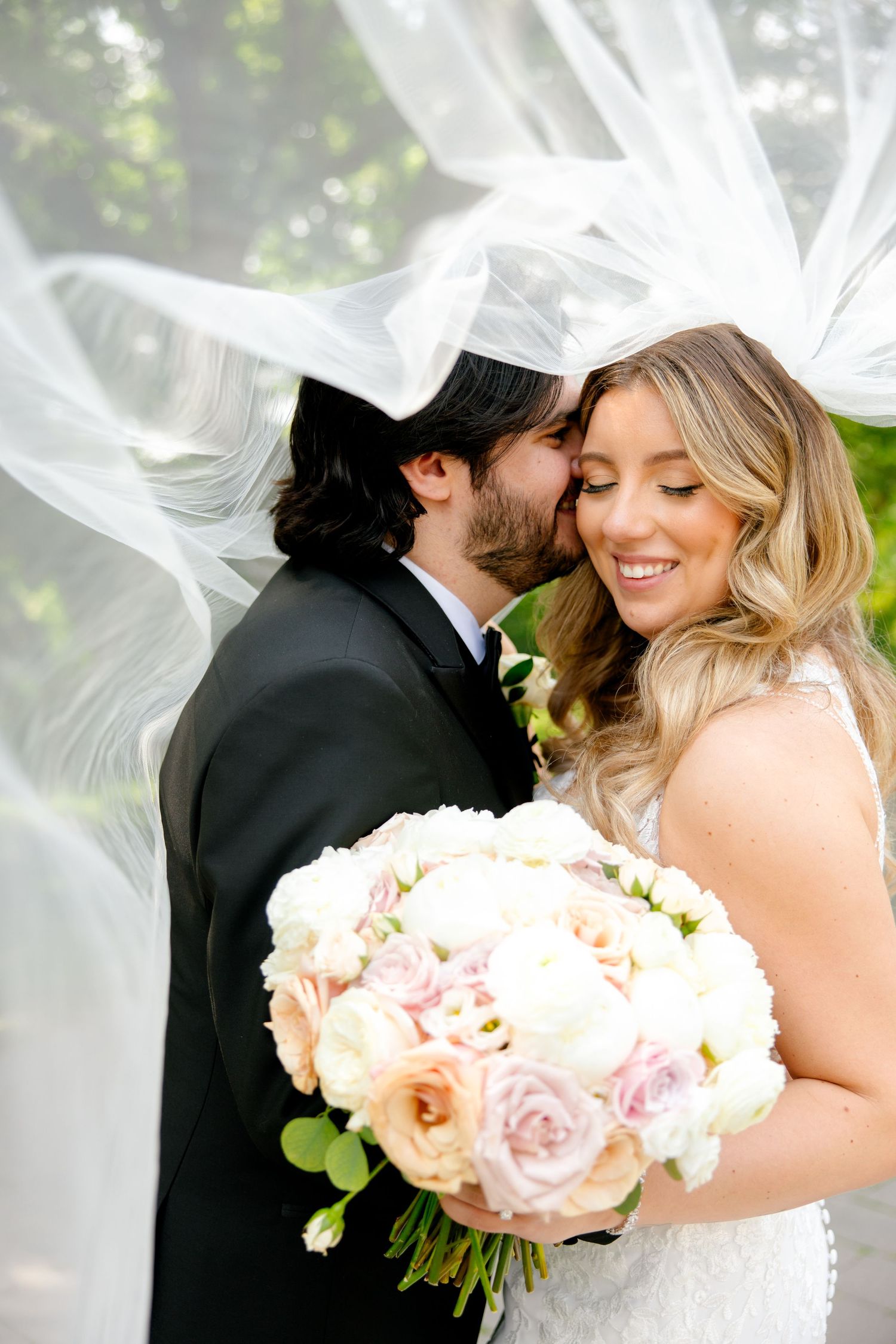 A romantic moment captured with flowing veil and soft pink rose bouquet in a garden setting.