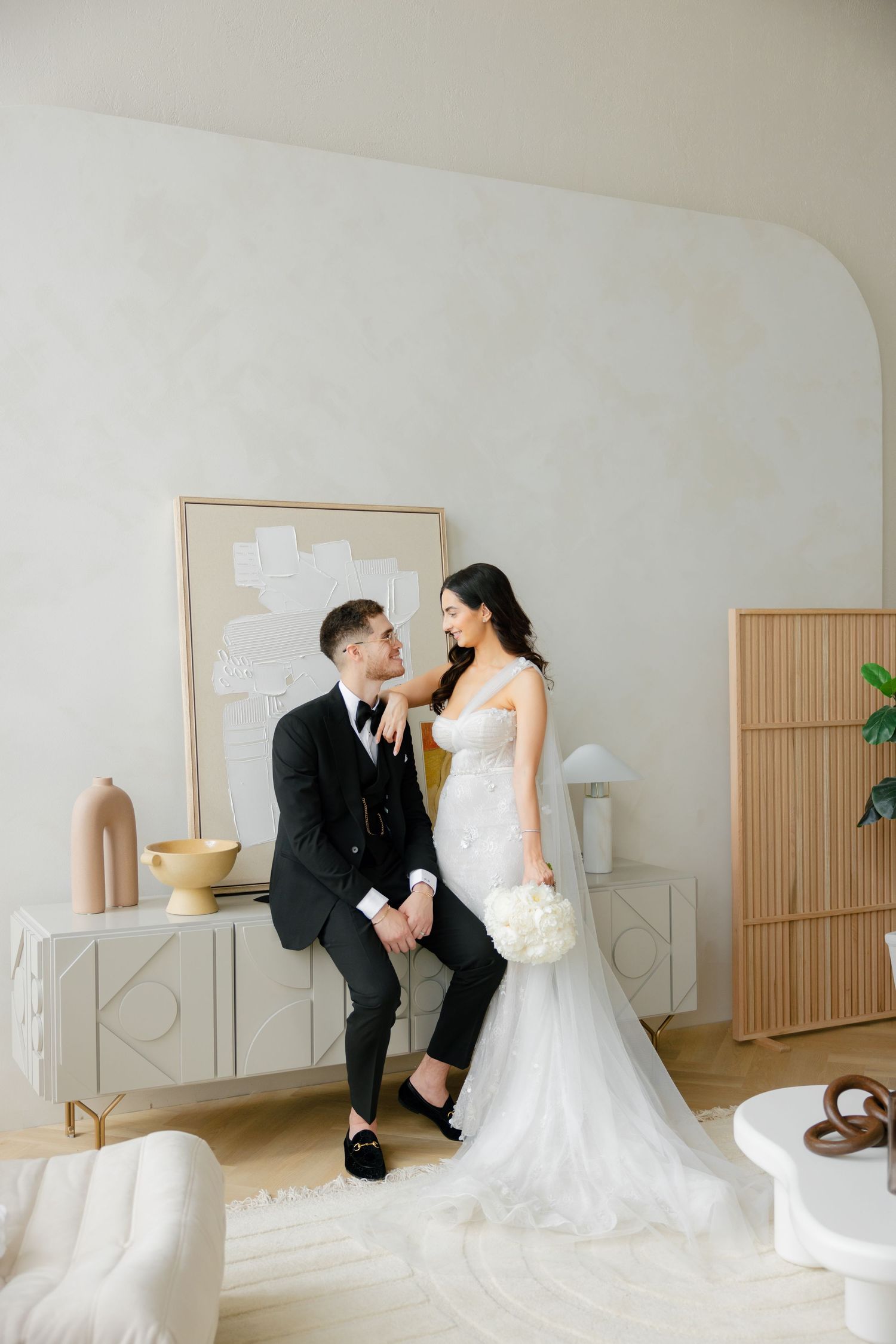 Candid moment between newlyweds sitting on sleek modern furniture in bright white room.