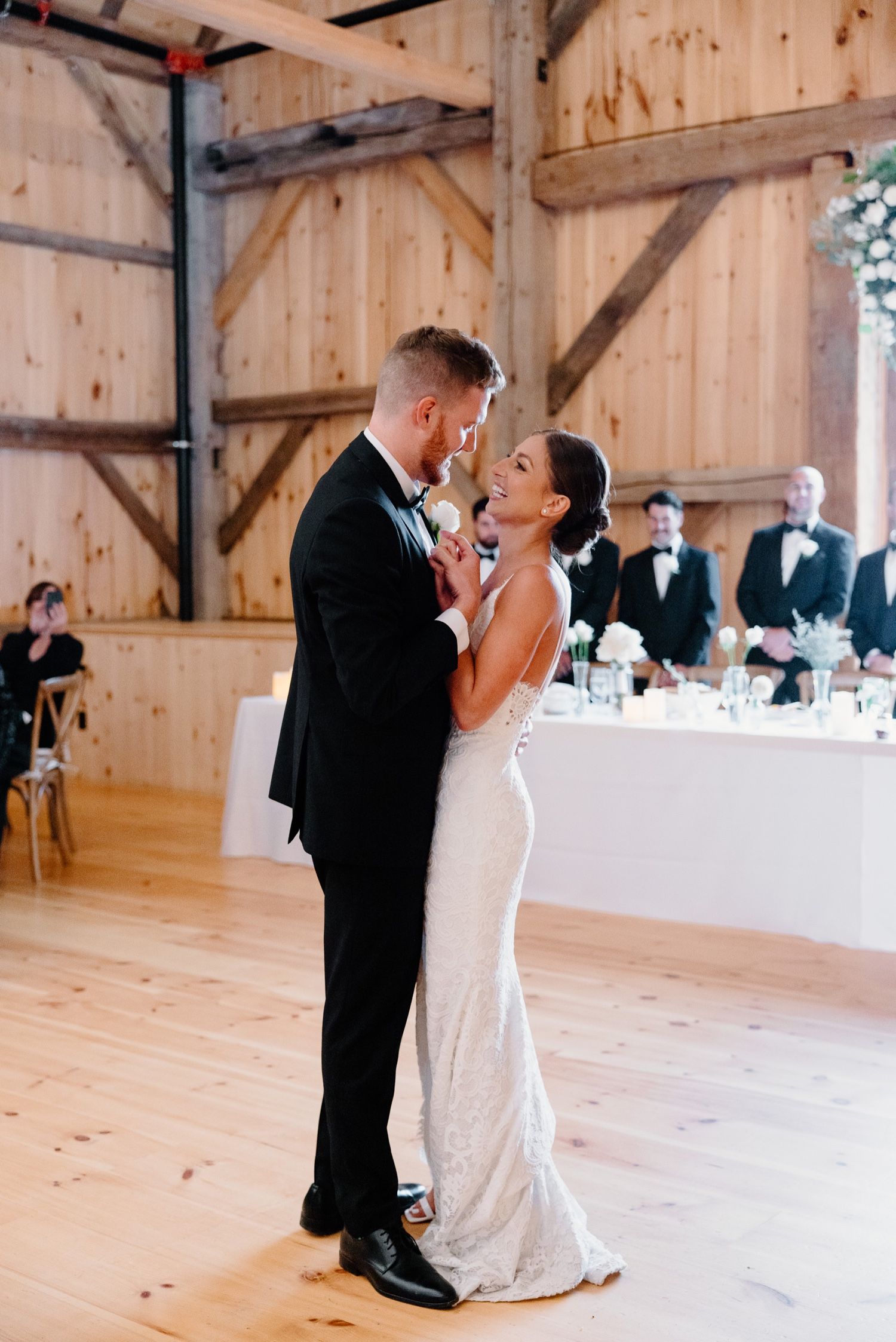 Couple shares an intimate dance moment in a wooden barn reception venue with guests seated in background.