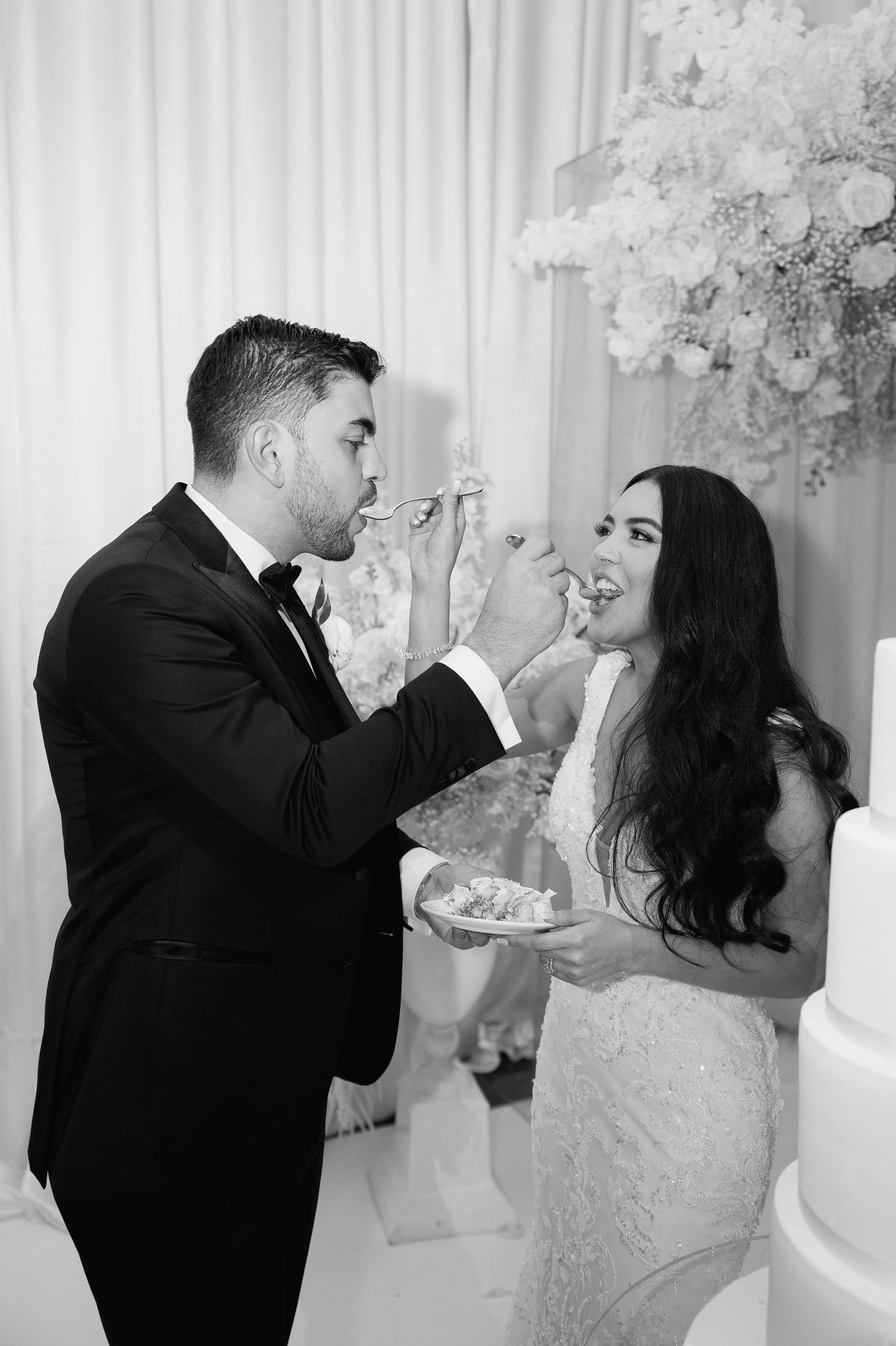 Black and white photo of couple playfully sharing wedding cake at their reception.