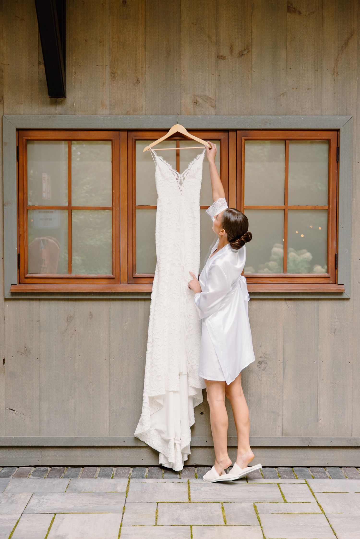 White wedding dress hanging on display while being arranged against wooden windows.