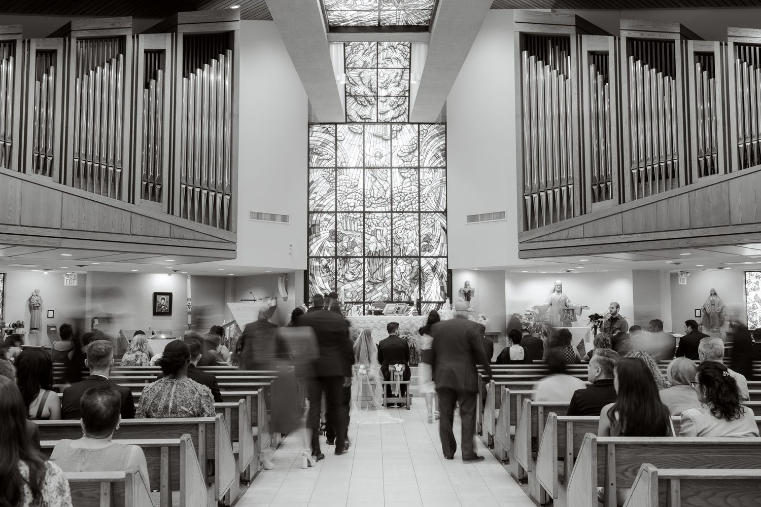 Black and white wide shot of church interior with pipe organs and guests seated in pews.