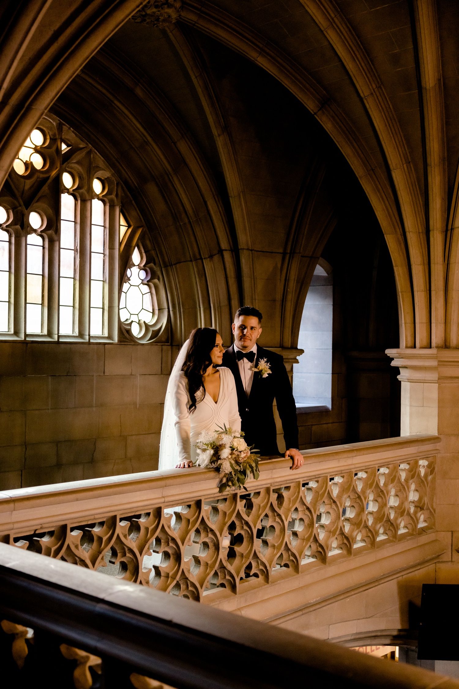Newlyweds pose against Gothic architecture with stained glass windows and stone arches.