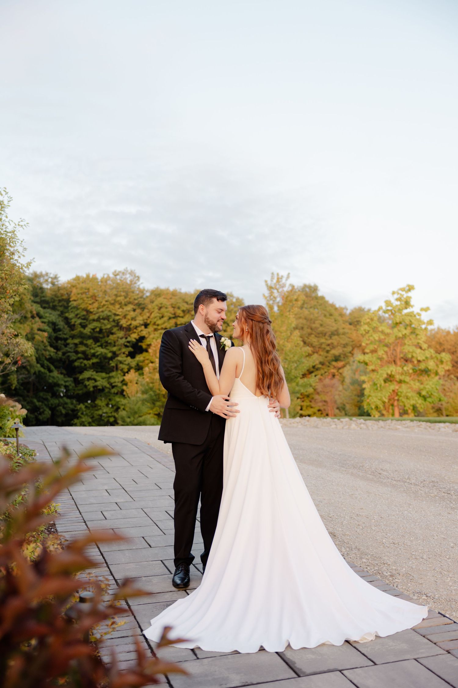 Newlyweds share an intimate moment outdoors against a backdrop of fall trees and cloudy skies.