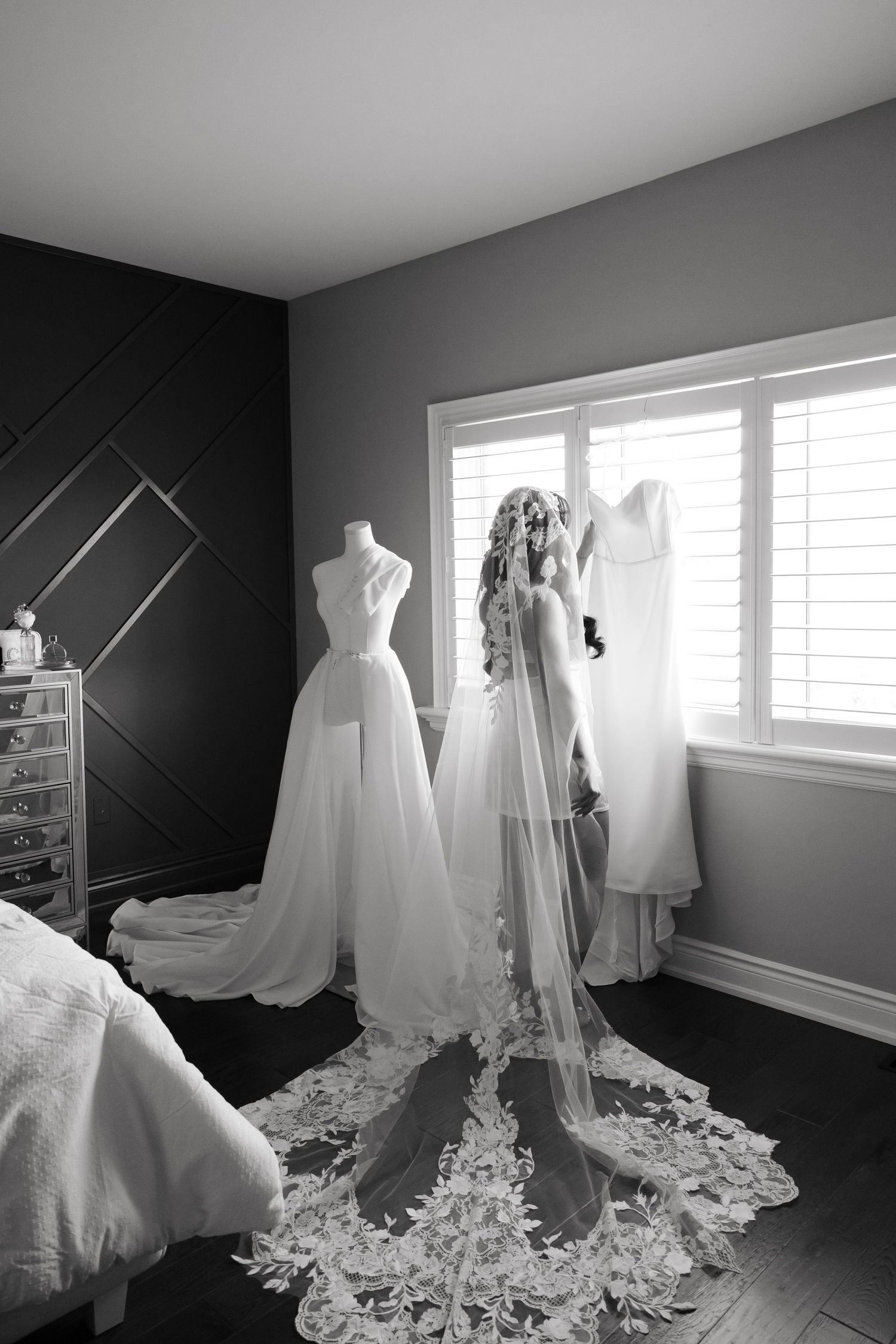 Black and white photo of bridal gowns and veils displayed in sunlit room.