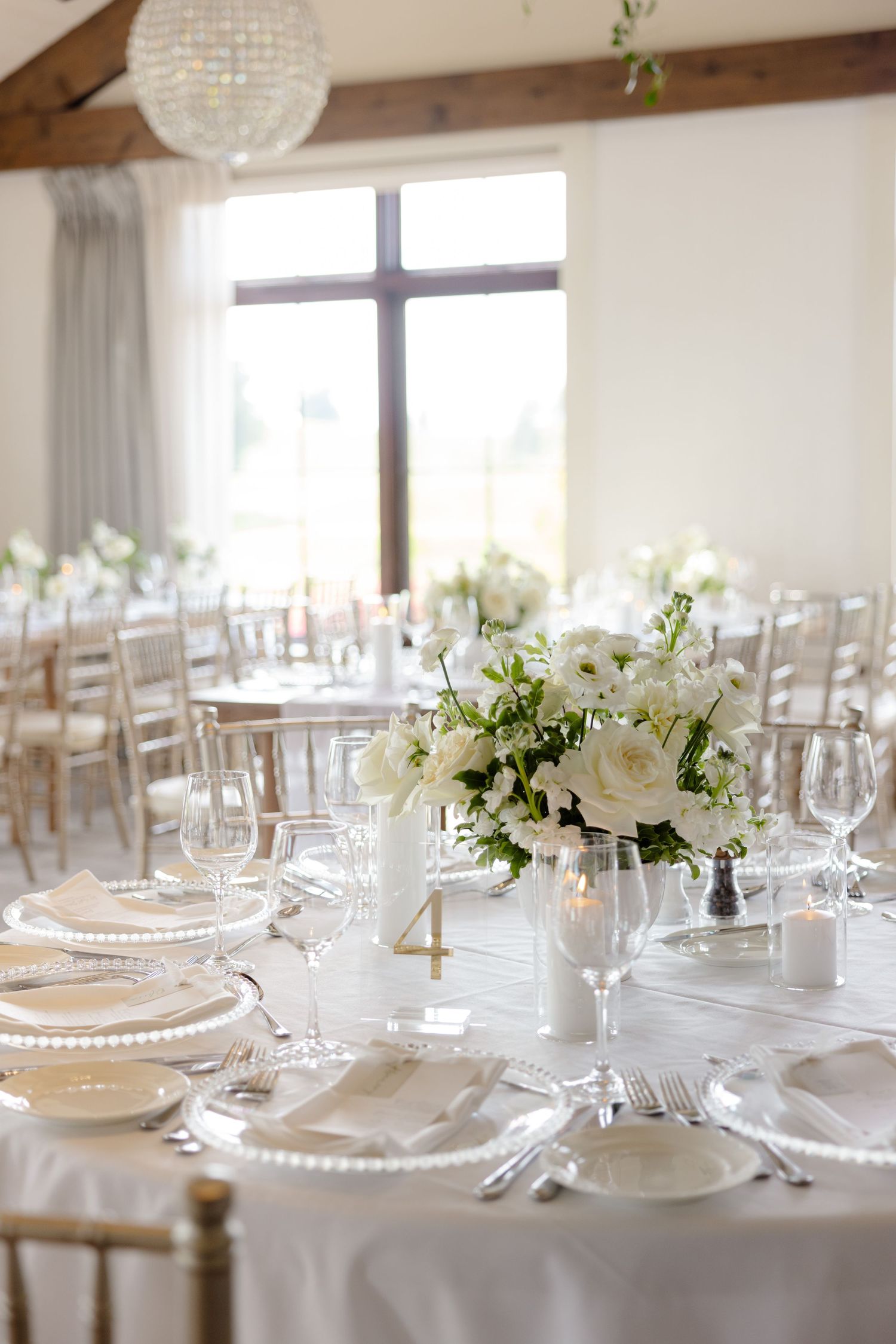 Bright wedding reception table with gold table number, white roses, and beaded charger plates.