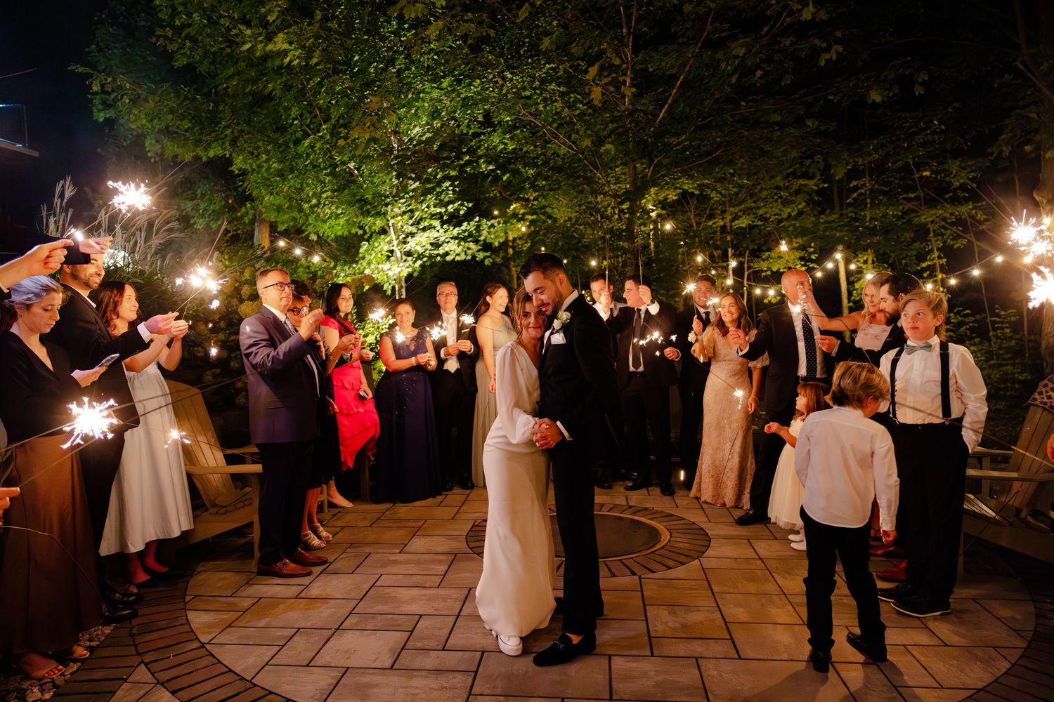 Guests with sparklers surround a dancing couple during an evening outdoor wedding celebration.