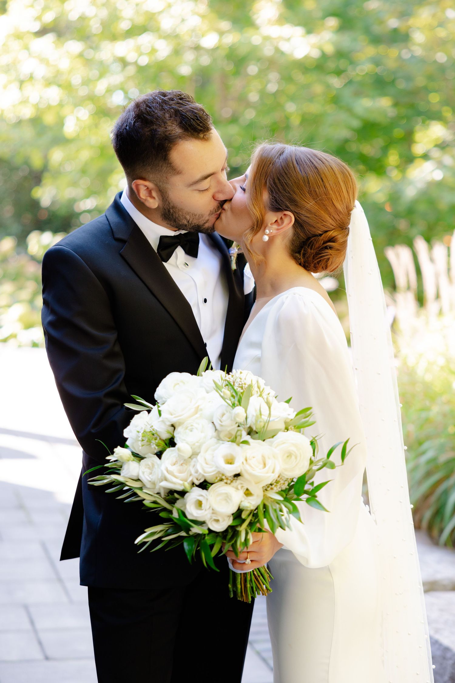 Romantic wedding kiss captured in a garden setting with white floral bouquet.