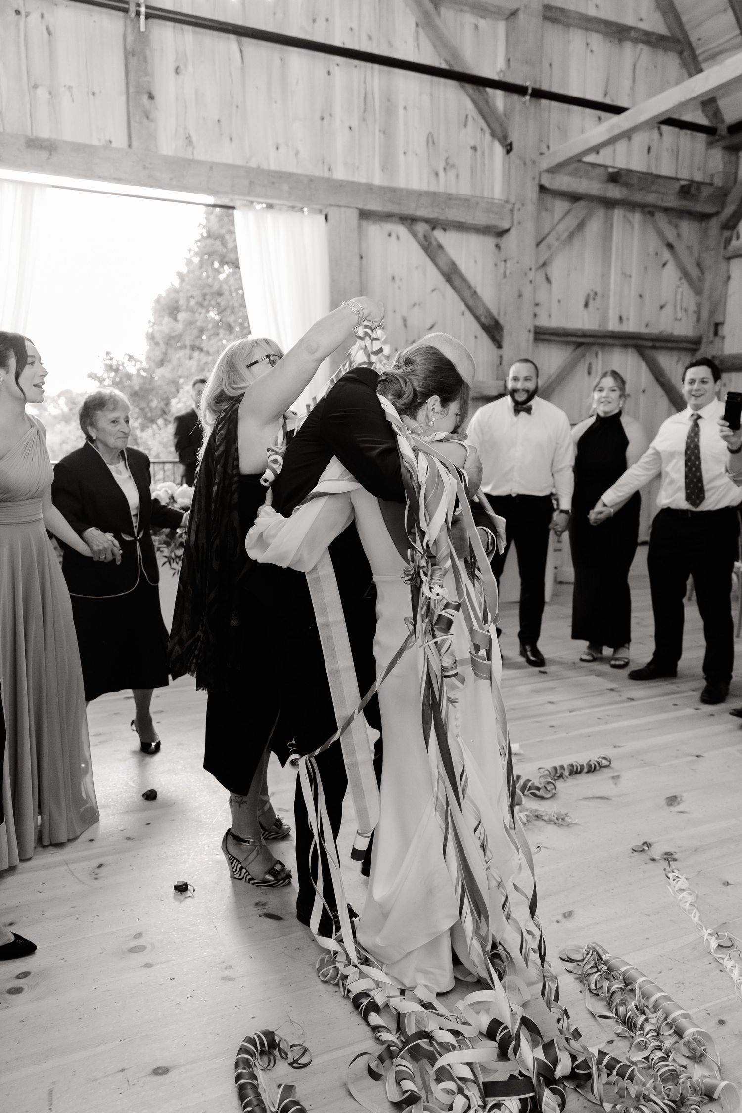 Black and white photo of wedding celebration with dancing and streamers in rustic venue.