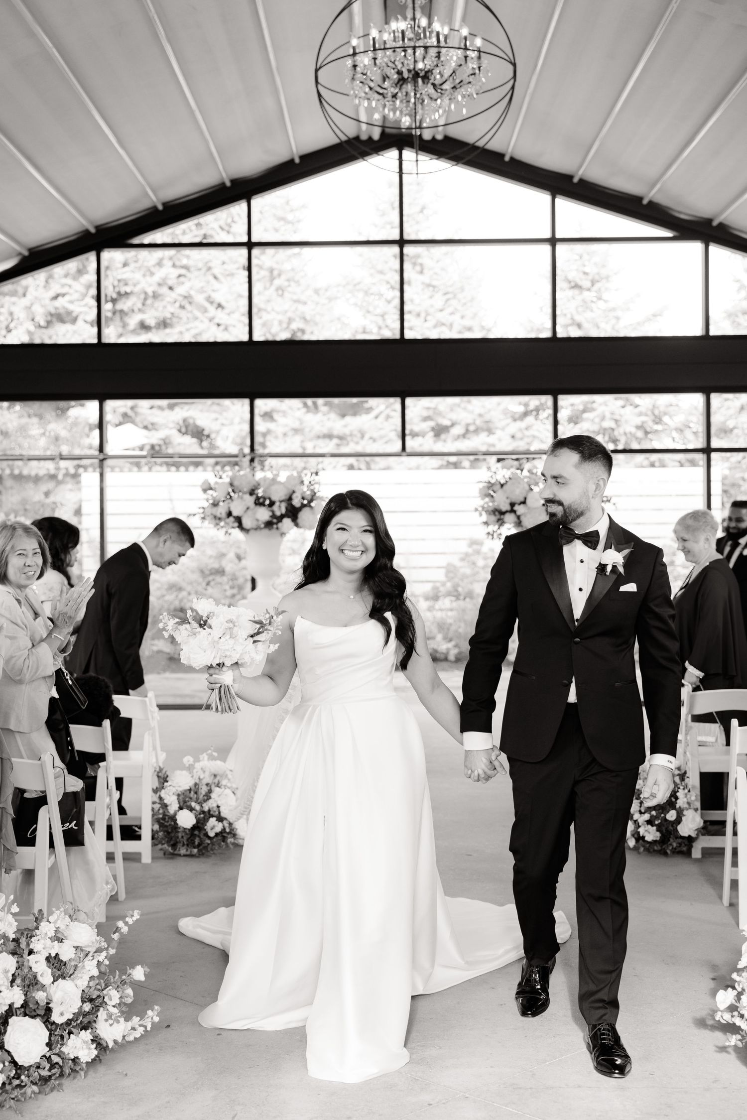 A joyful wedding ceremony exit down the aisle in a bright venue with floor-to-ceiling windows.