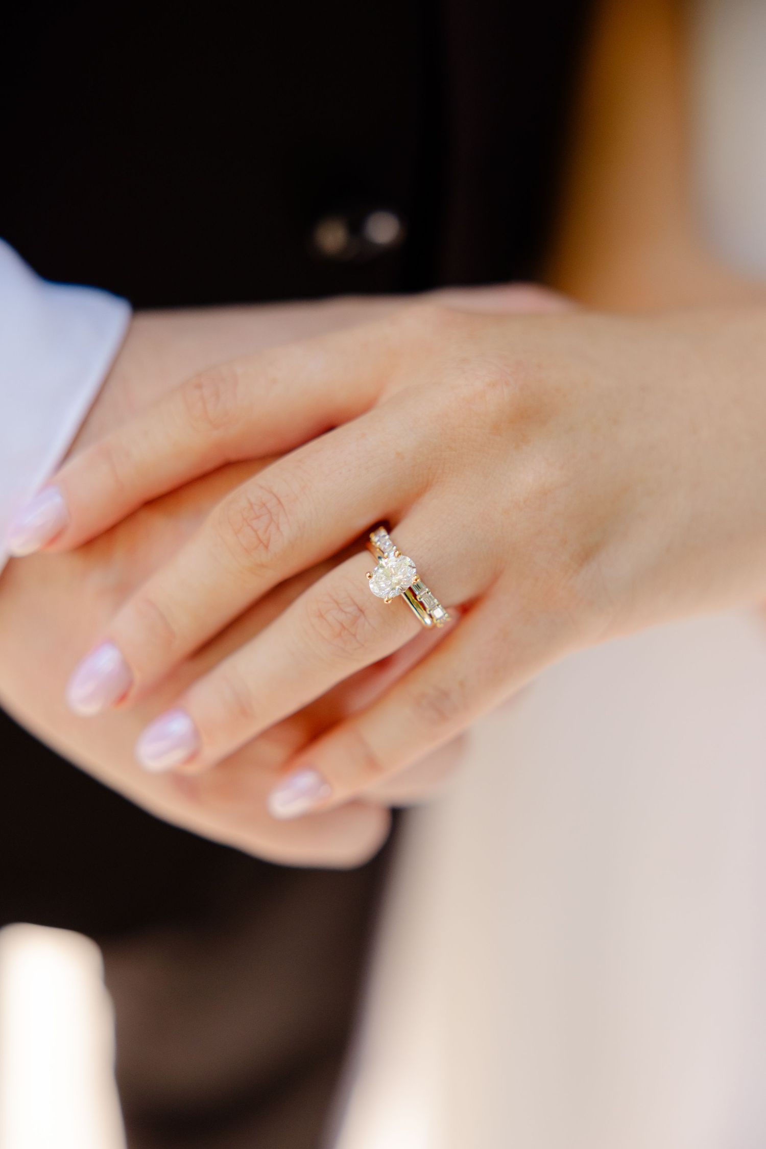 Close-up of an elegant diamond engagement ring on a manicured hand against white fabric.