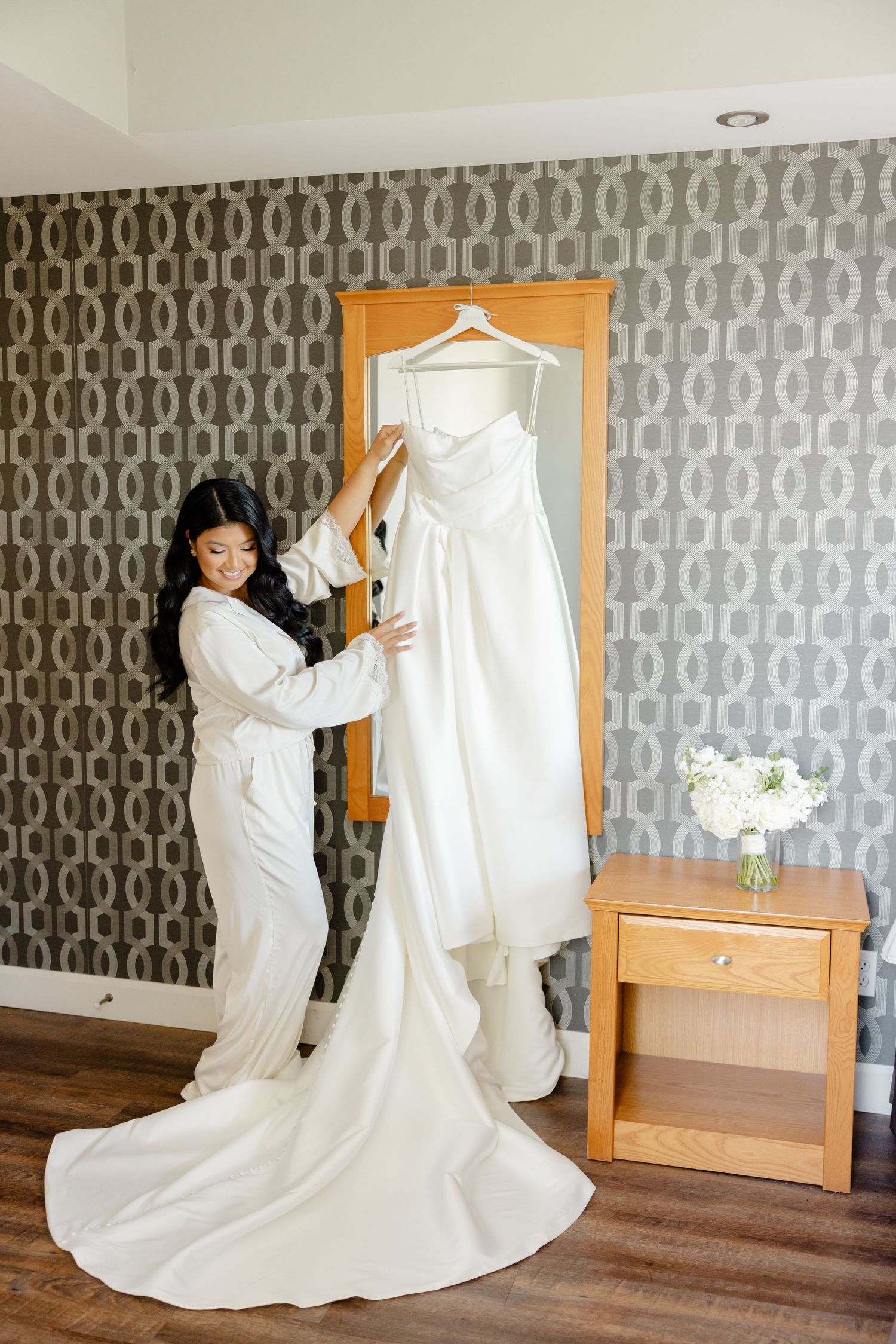 Wedding dress preparation scene with white gown displayed against geometric wallpaper.