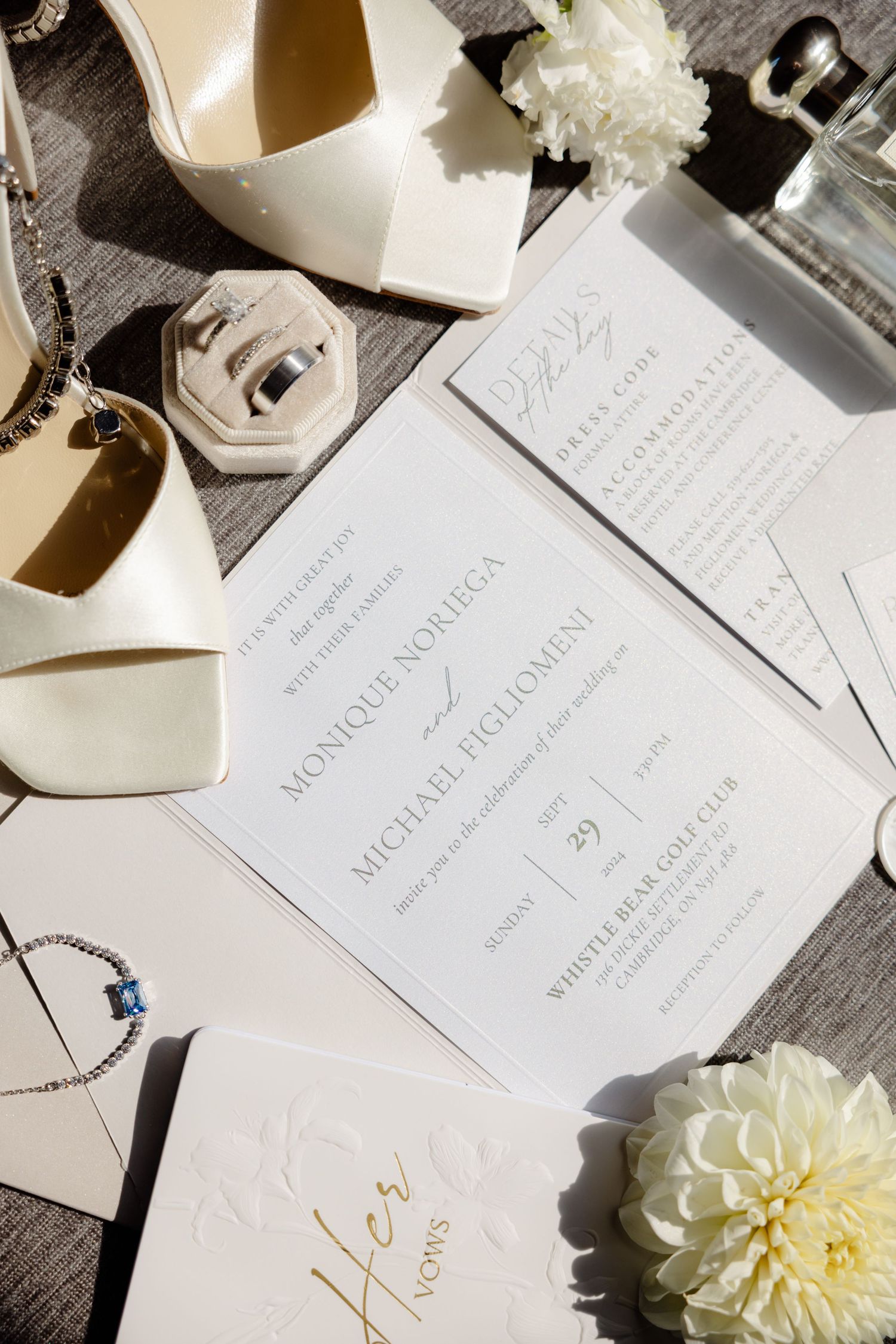 Elegant wedding invitation suite with white flowers, Jimmy Choo shoes and ring box on dark wooden surface.