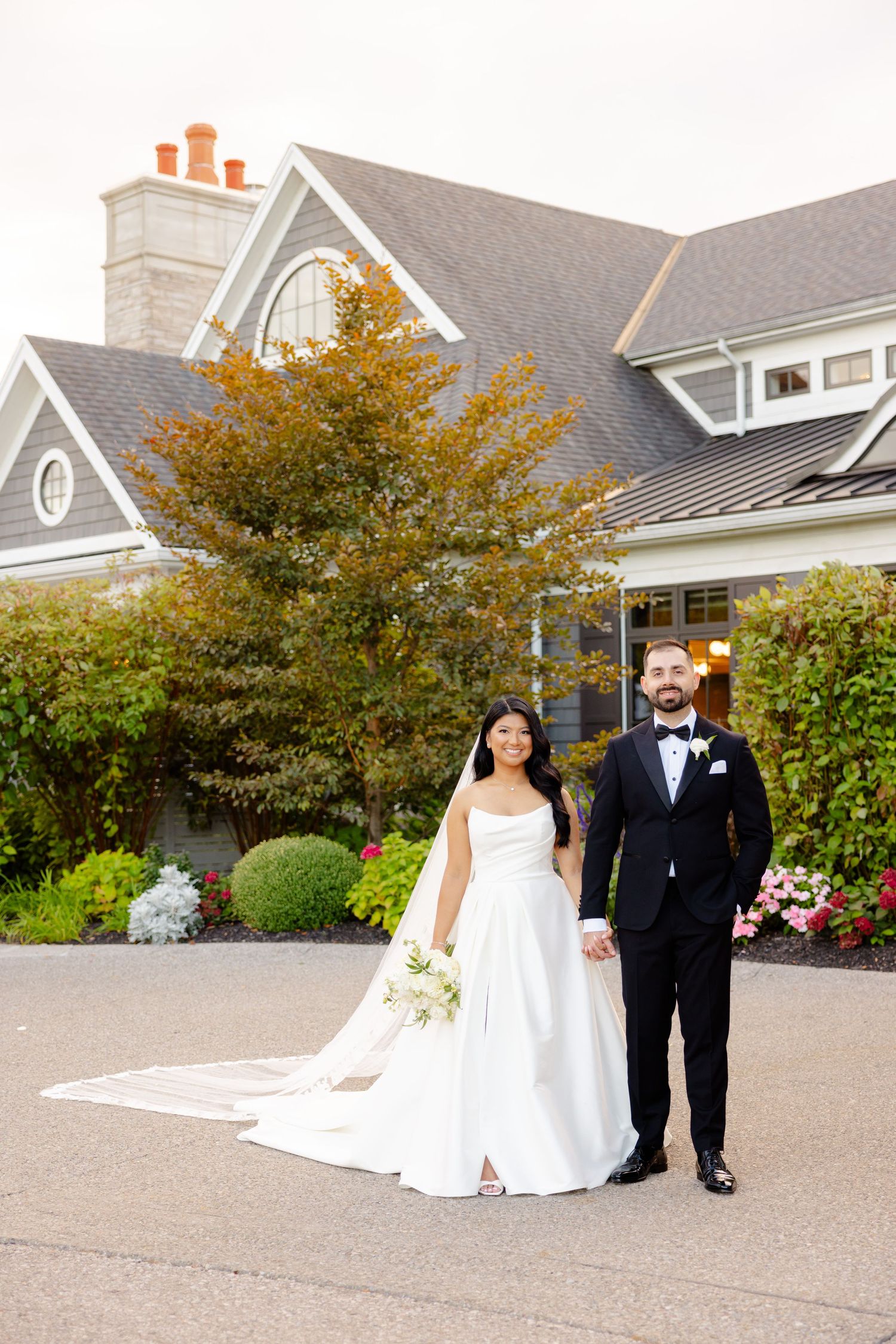 A wedding couple poses formally in front of a luxurious venue with fall decor.