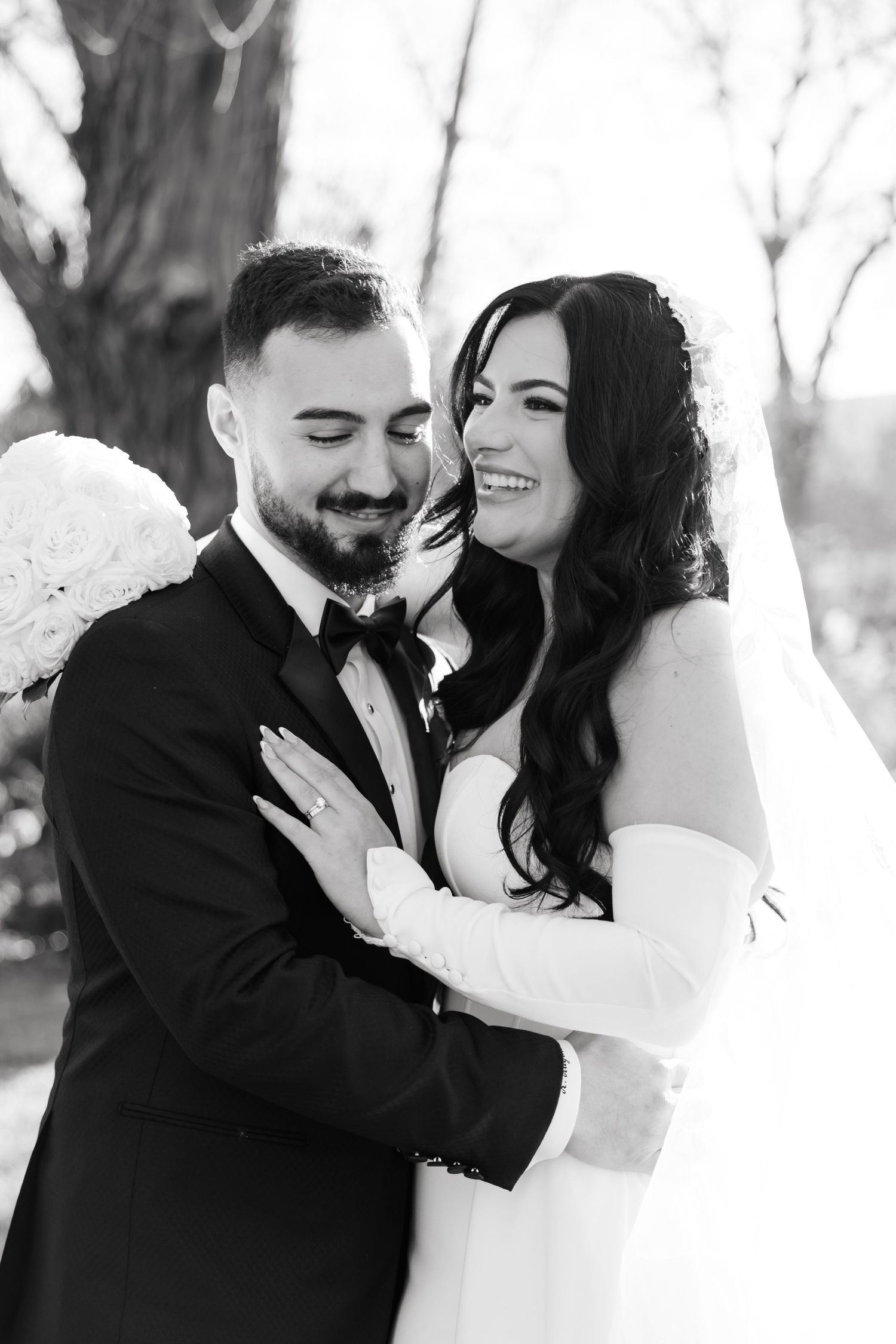 A romantic black and white wedding photo of a couple embracing and smiling outdoors.