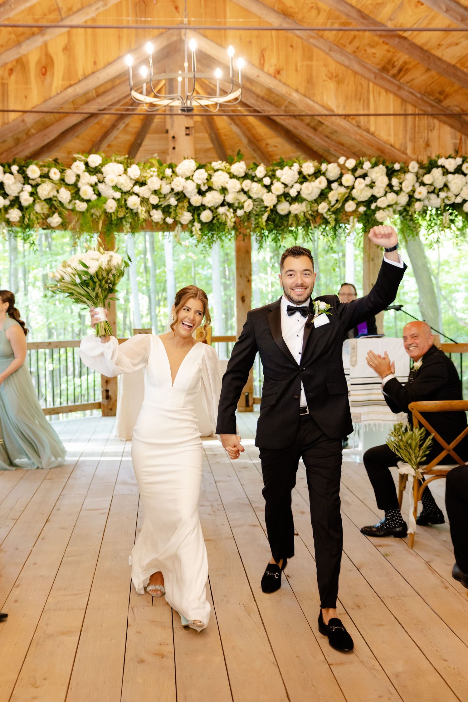 Celebratory wedding exit in a rustic wooden pavilion decorated with white flowers and greenery.