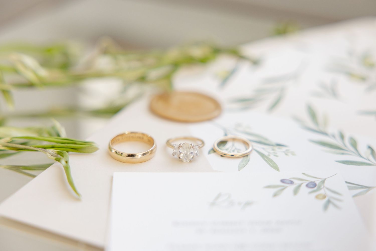 Gold wedding bands and diamond engagement ring displayed on white invitation with botanical details.