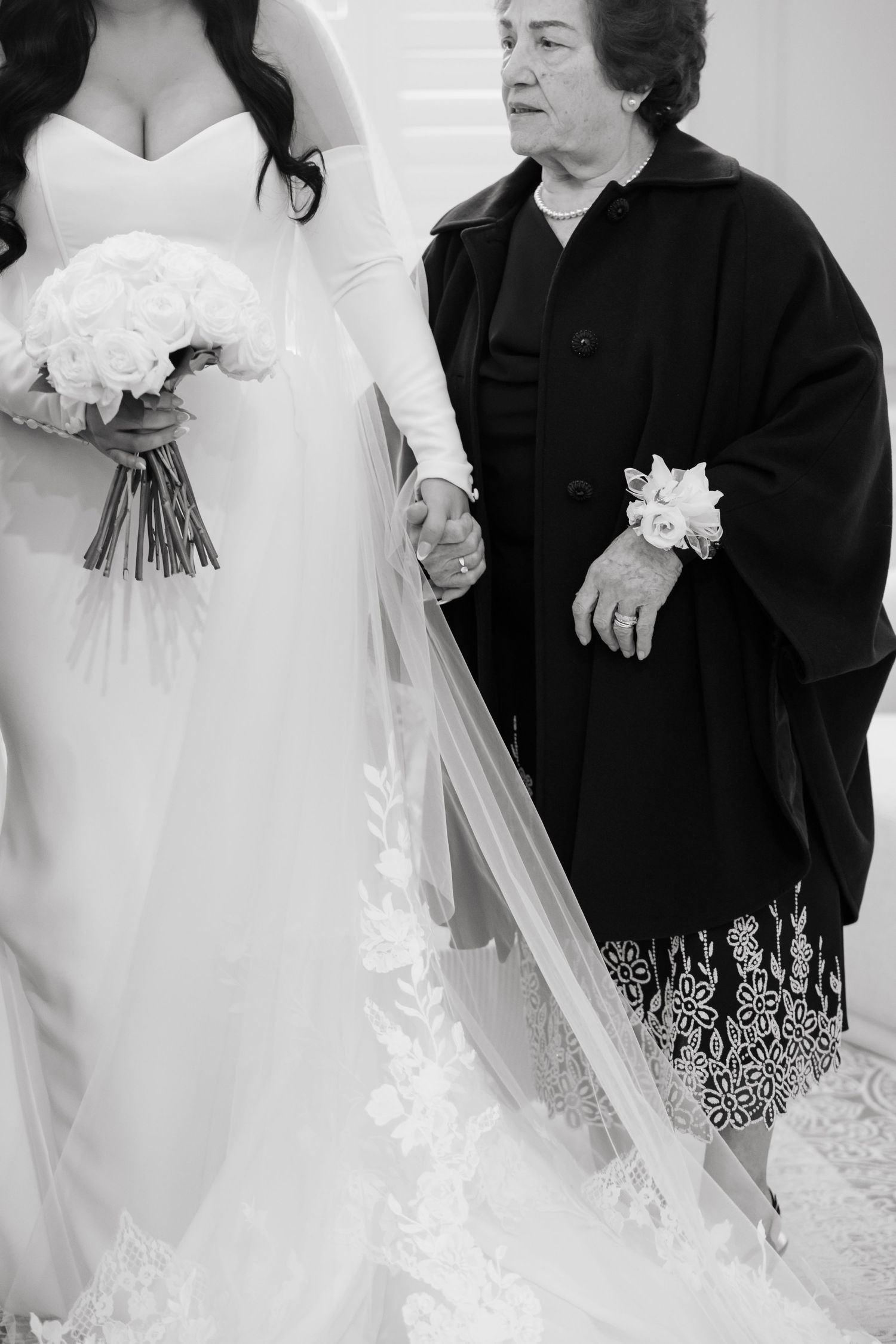 Close-up black and white photo of bride in white dress holding bouquet and sharing moment with wedding guest.