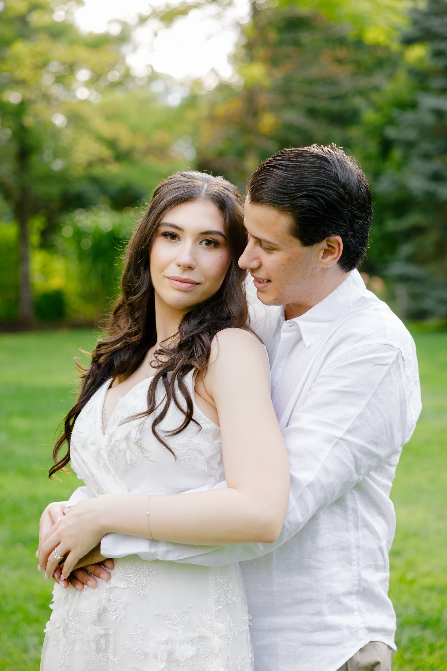 Natural light portrait of couple in white clothing embracing in lush garden setting.