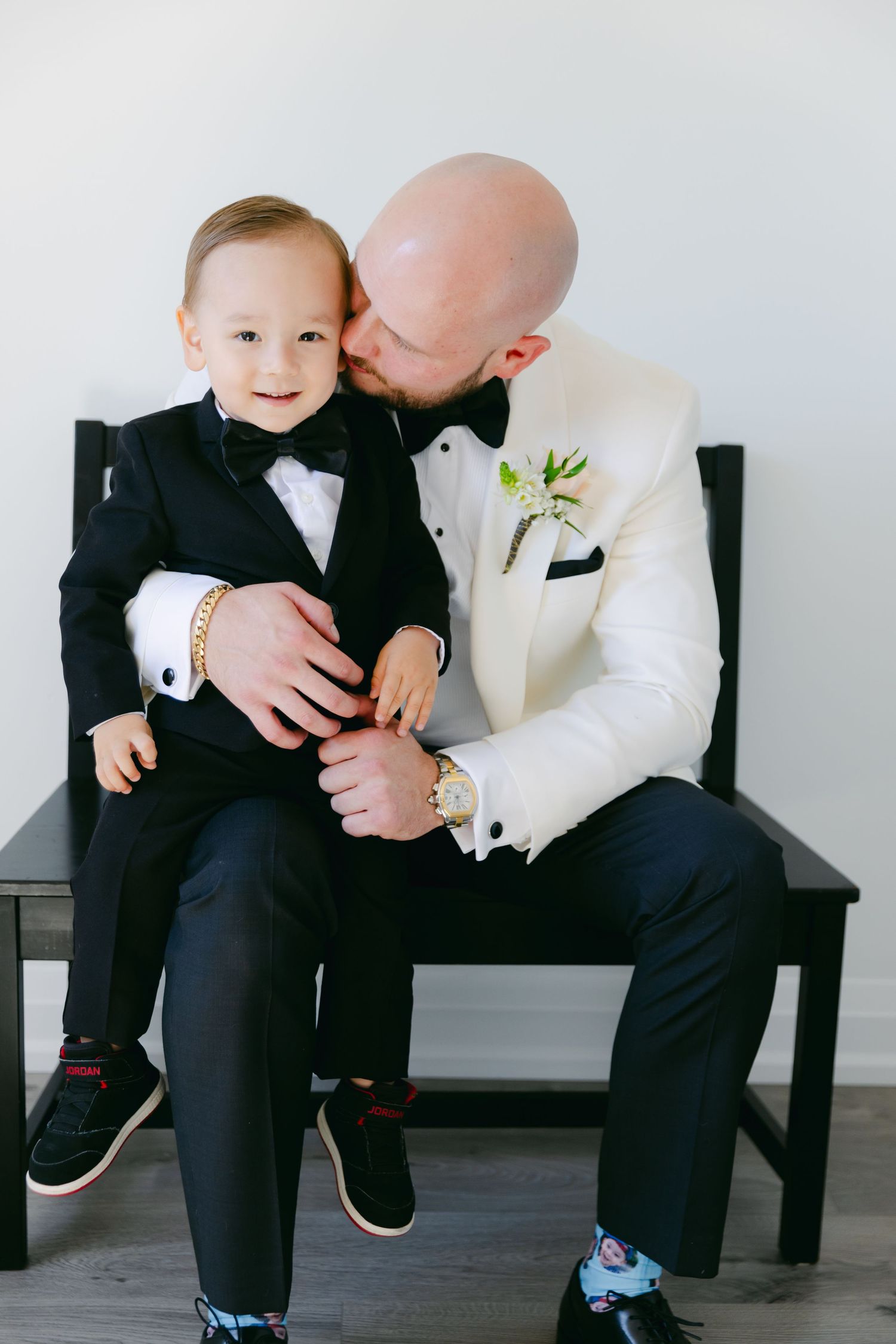 A touching moment captured of a small boy in a tuxedo sharing a tender moment on a wooden bench.