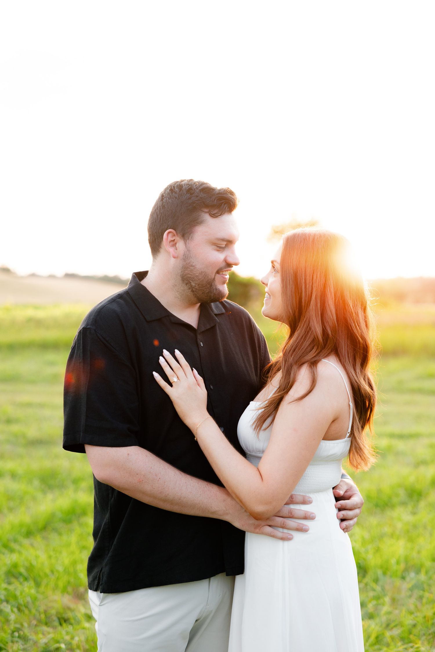 A couple embraces in a sunlit field during their engagement photoshoot.