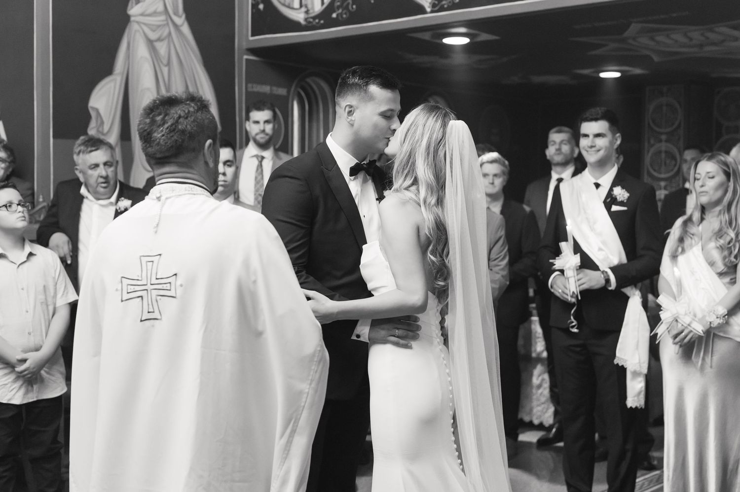 Black and white photo capturing tender moment during traditional Orthodox wedding service.