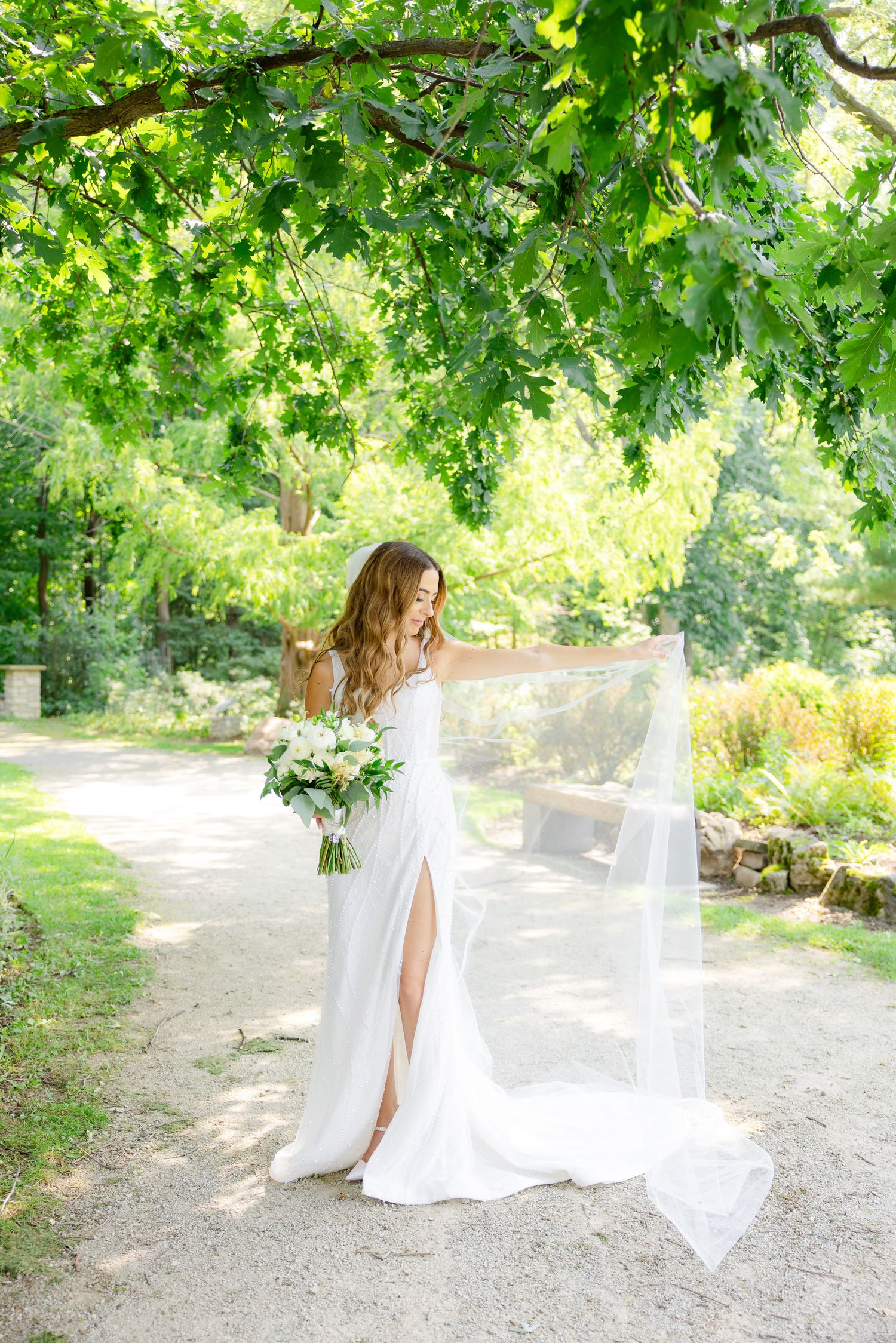 A garden wedding portrait featuring flowing white dress and veil with lush green backdrop.