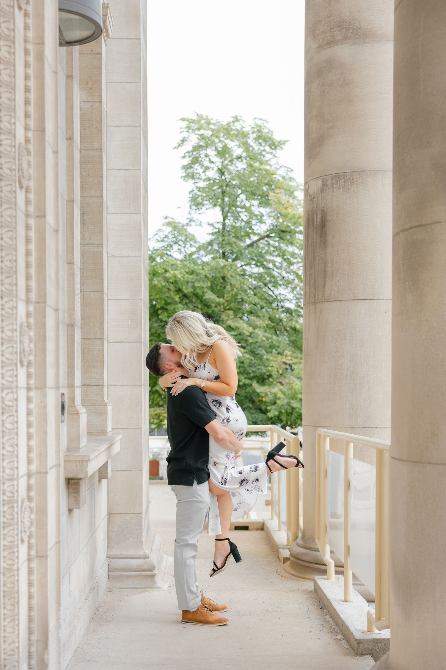 A dramatic lift pose between elegant stone columns with greenery in background.