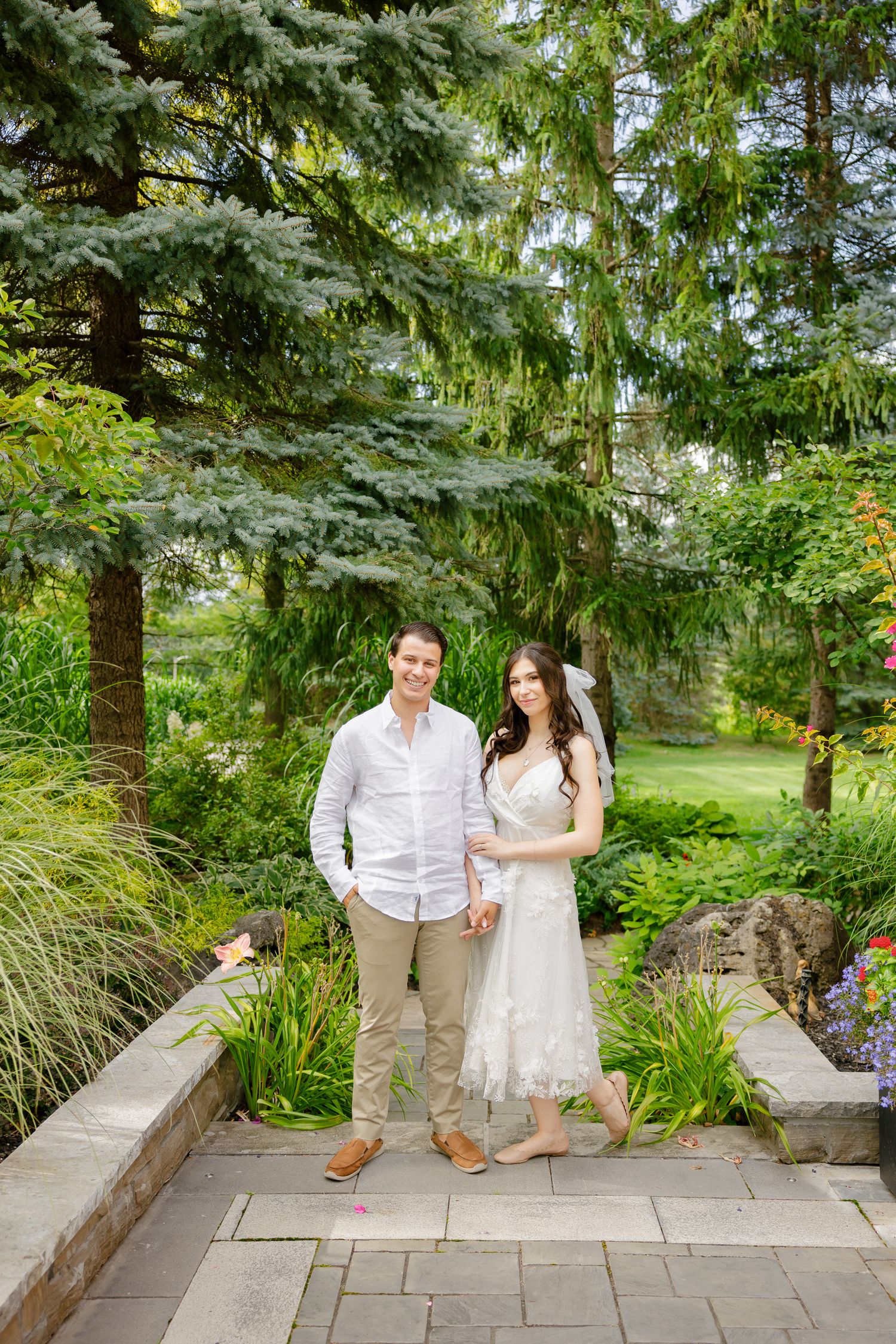 Garden wedding portrait on stone pathway with evergreen trees in background.