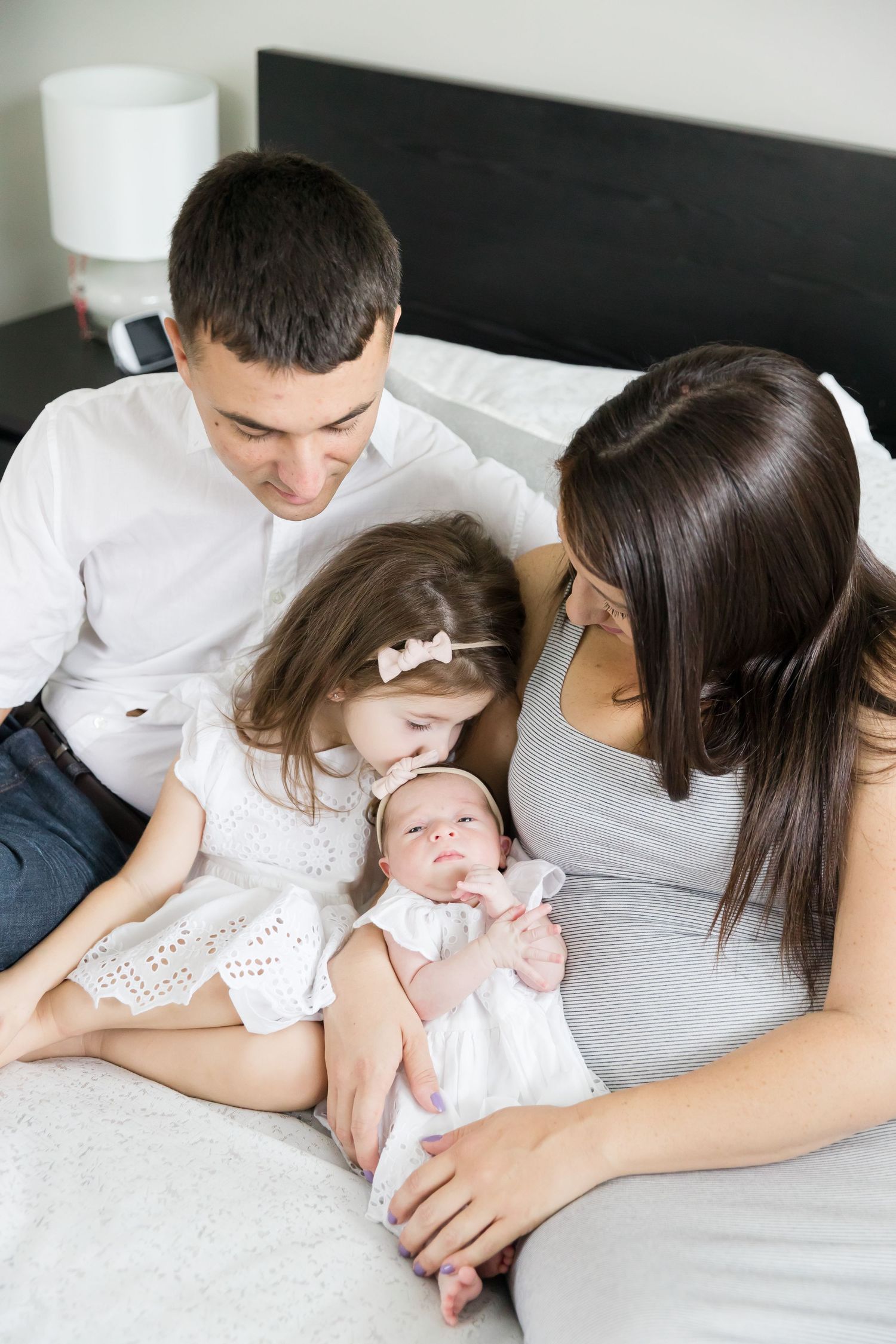 Family gathered on bed looking lovingly at newborn baby.