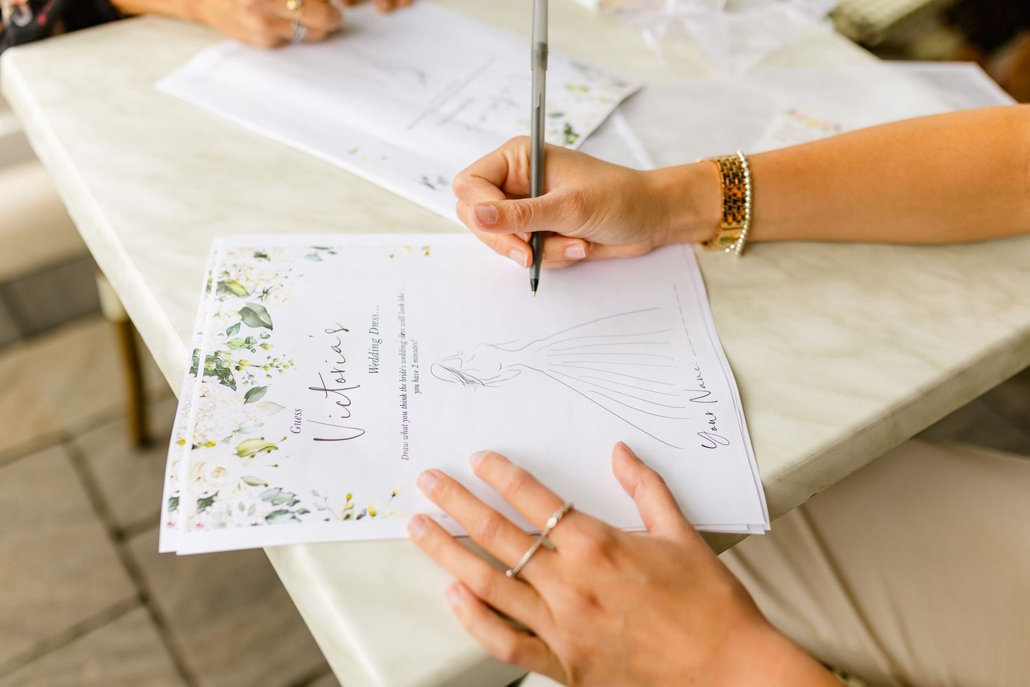 Close-up of hands writing on decorative paper with floral designs.