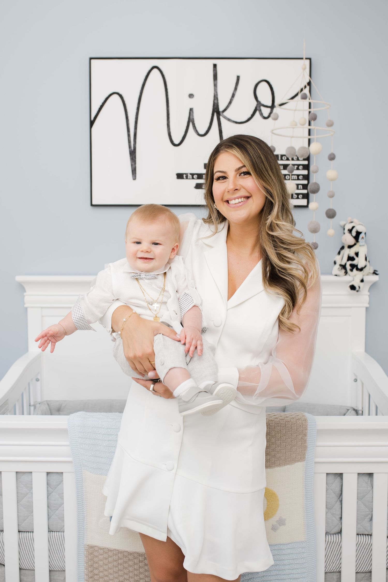Baby and adult pose in front of nursery wall art in white room.