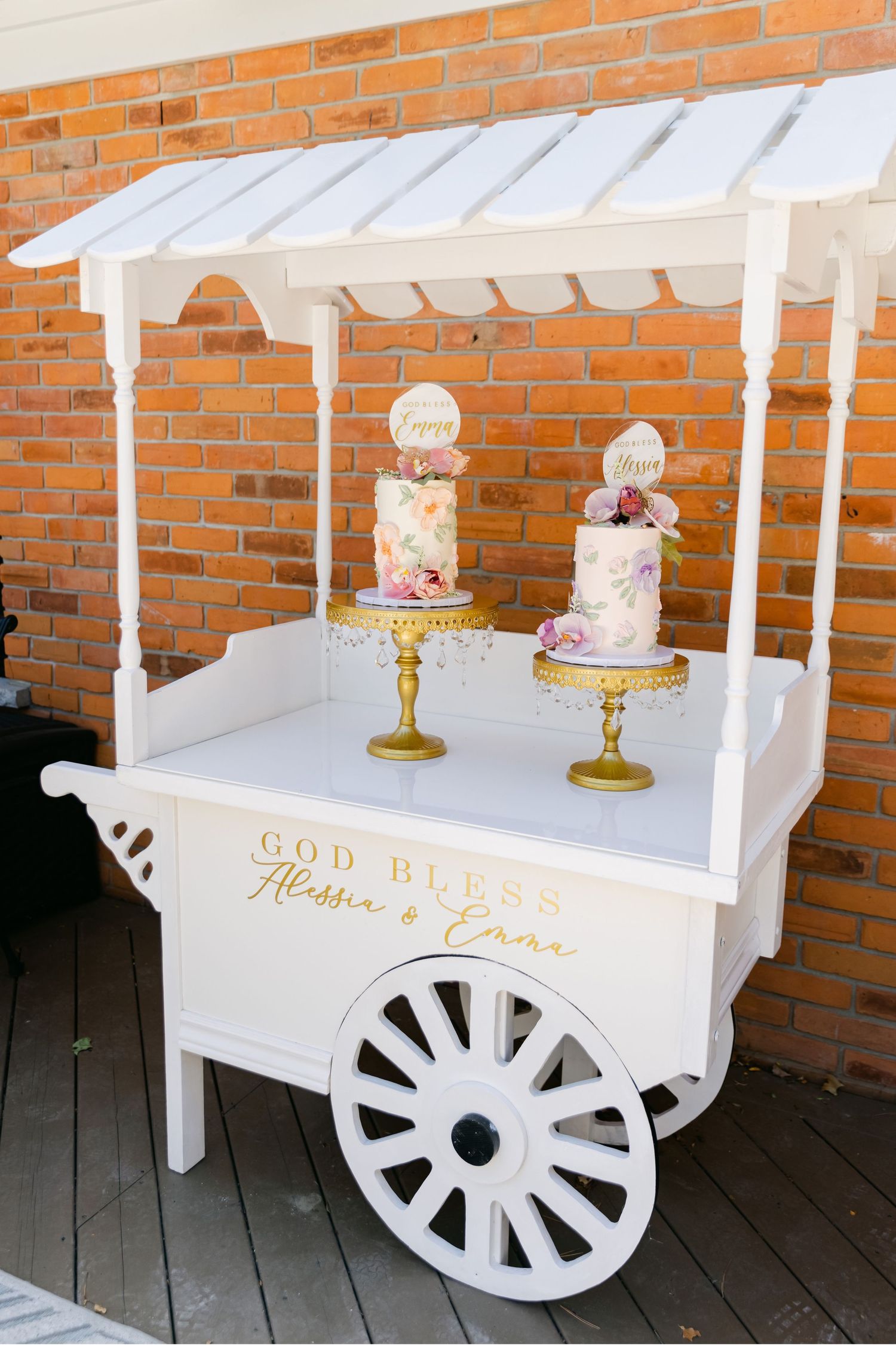 White vintage-style dessert cart with 'God Bless' inscription displaying two elegant tiered cakes.