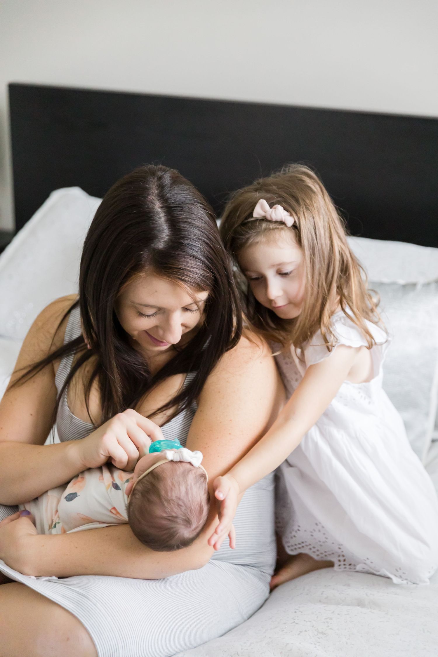 Family sharing tender moment while caring for newborn on bed.