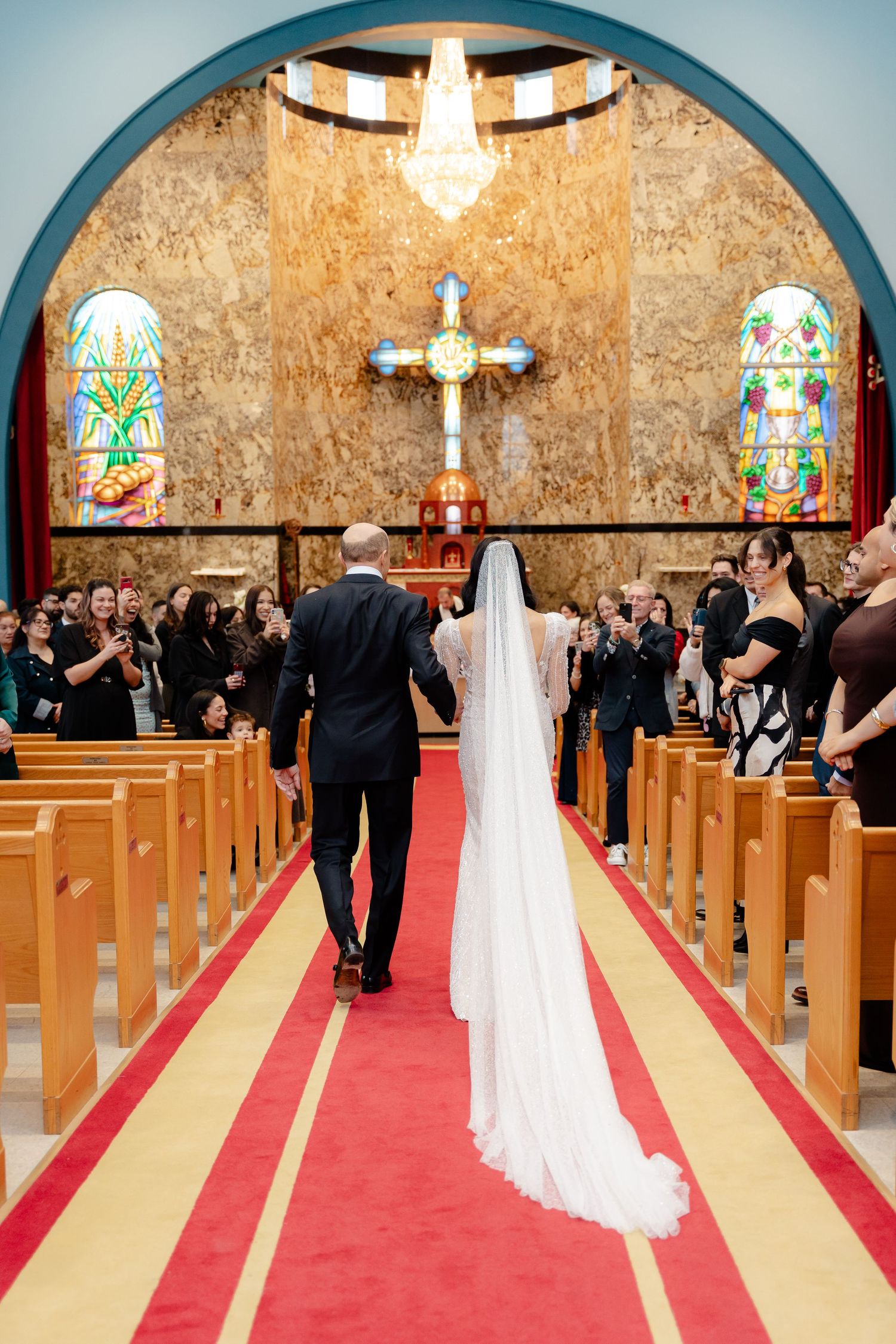 Wedding ceremony view down church aisle with long white veil and stained glass windows.