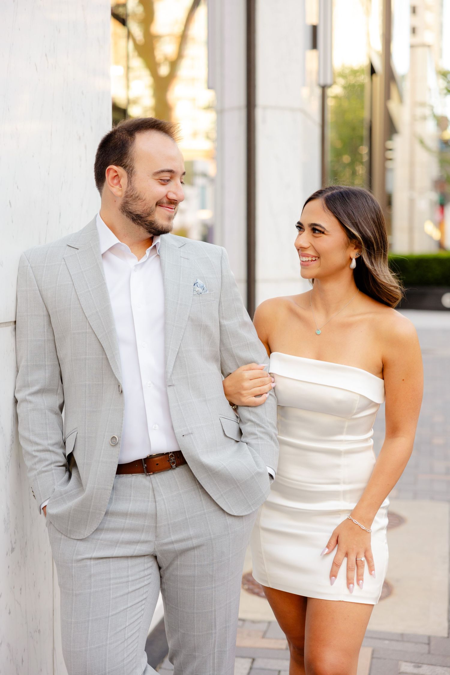 Happy couple sharing a moment while posing against white column outdoors.
