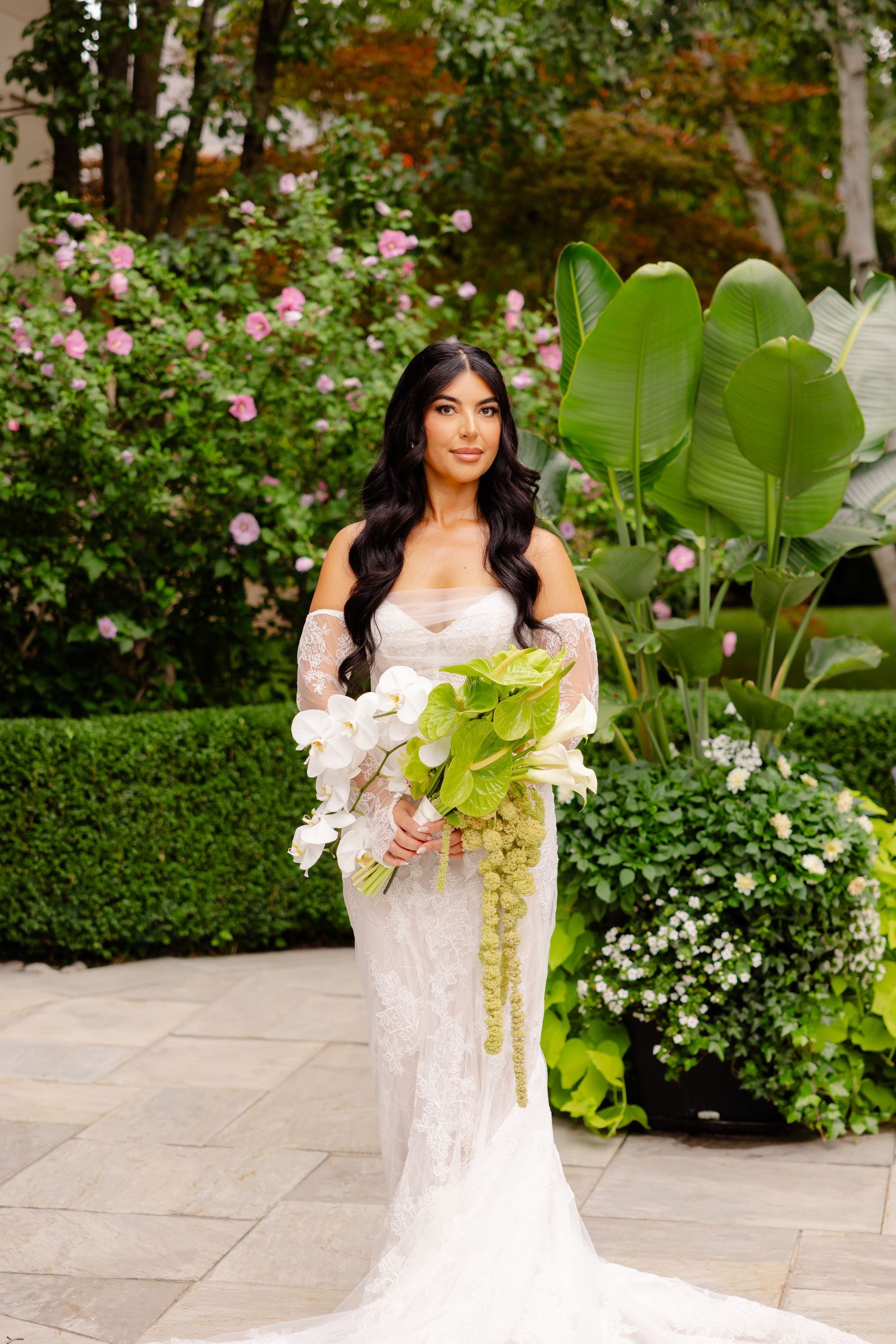 Bridal portraits in a garden setting showcasing a lace gown and tropical leaf bouquet.