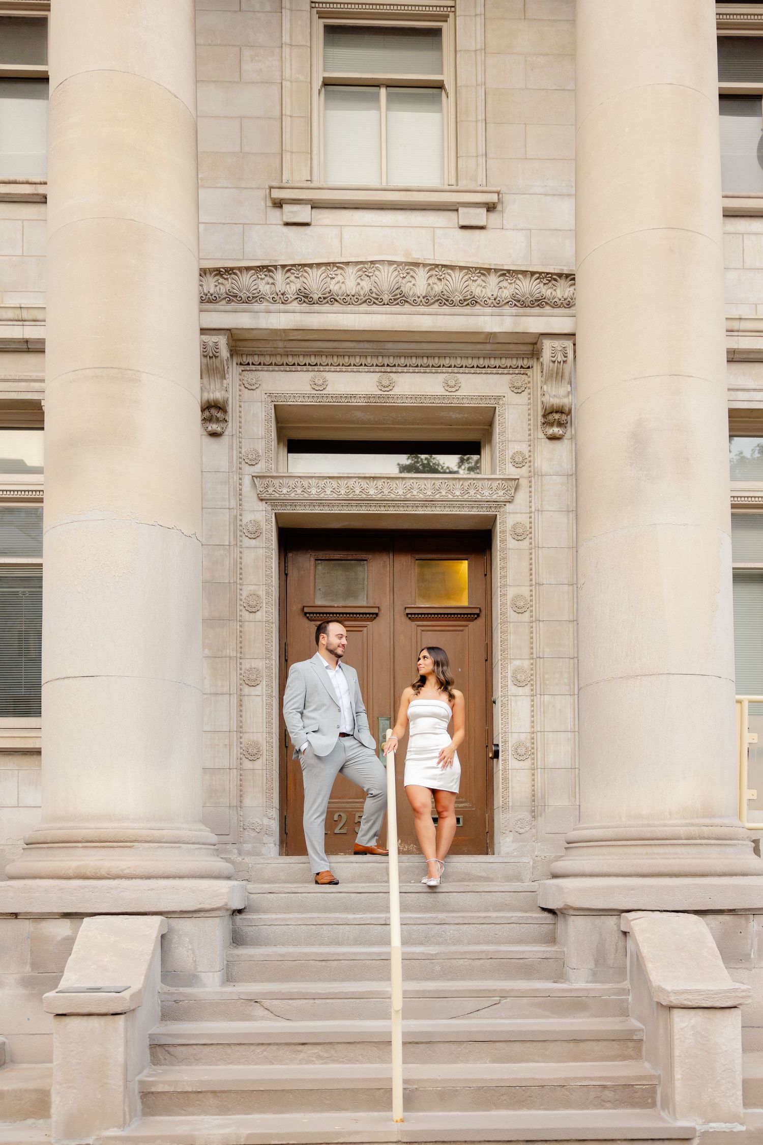 A couple poses in the entrance of a historic building with ornate architectural details.