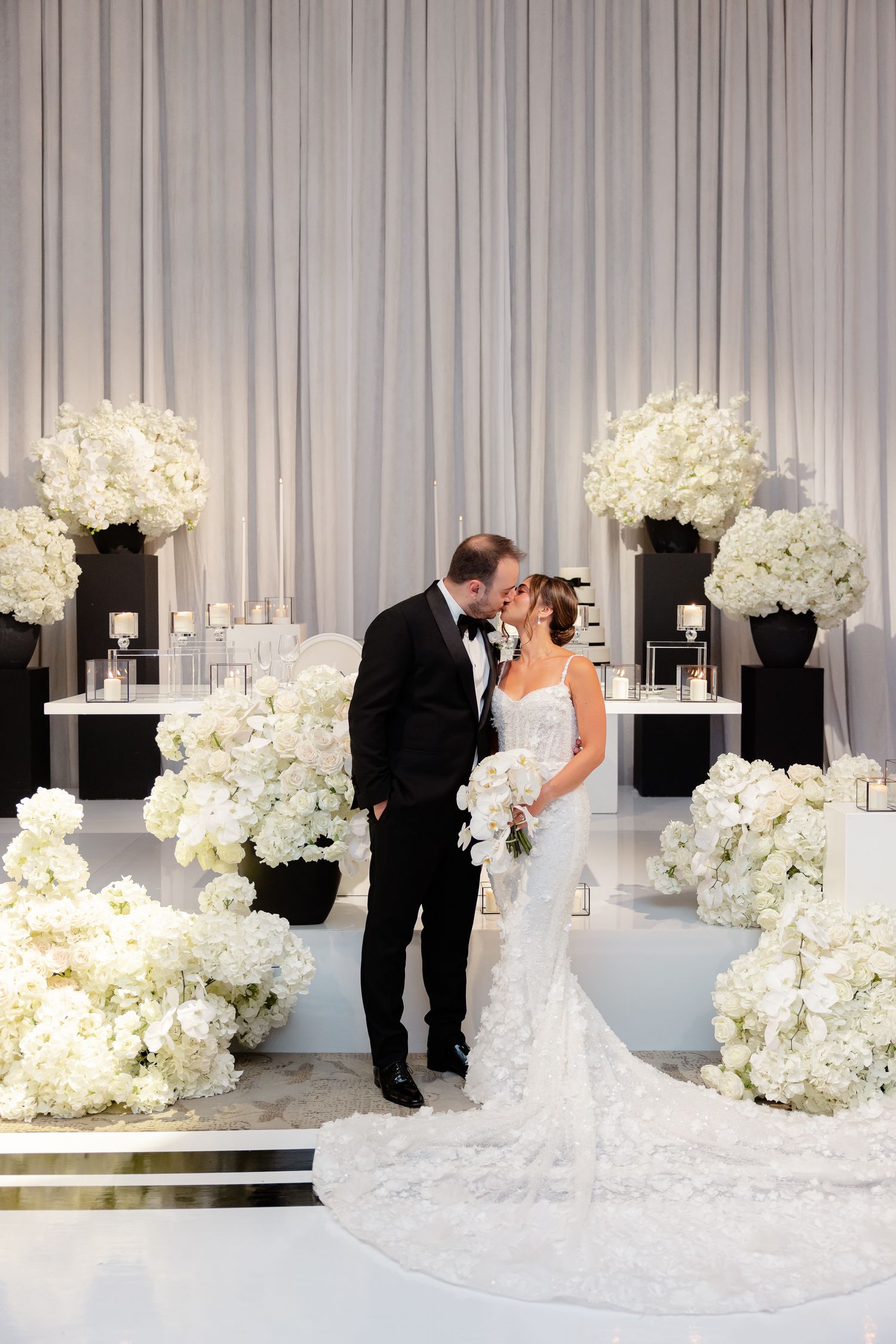 Elegant wedding ceremony setup with white hydrangea arrangements in black vases against a draped backdrop.