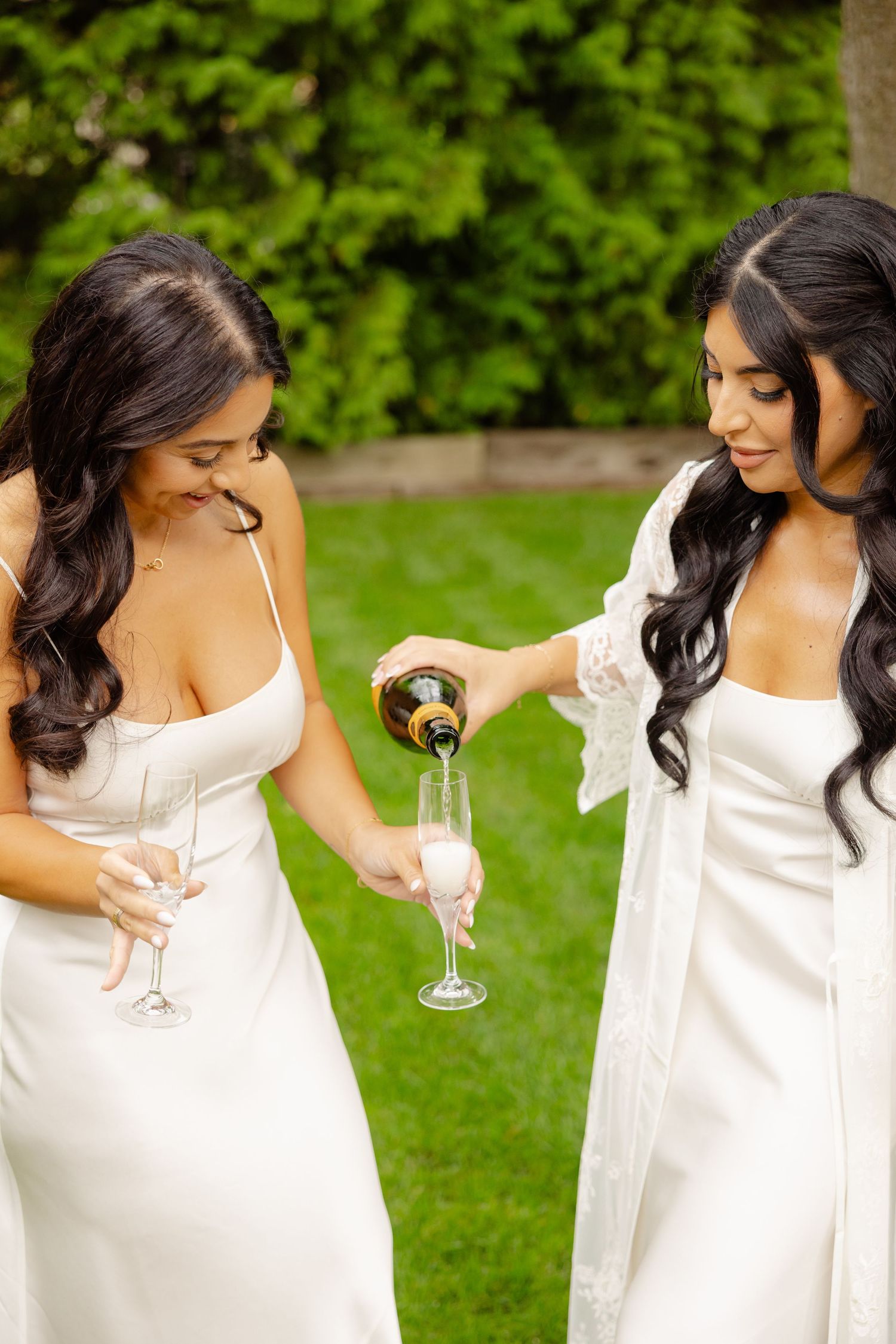 Friends in matching white outfits toast with champagne glasses against a green outdoor background.