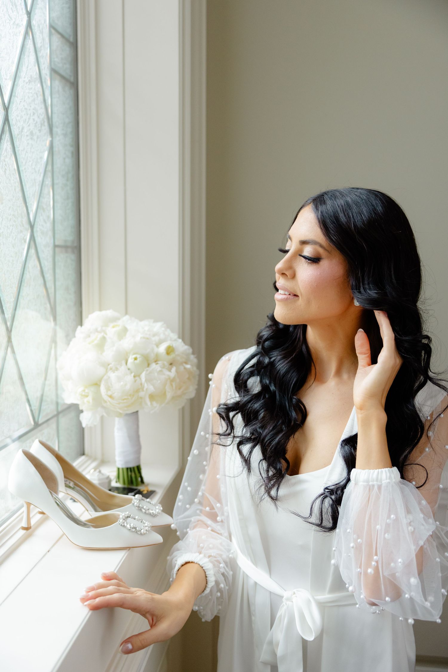 Elegant bridal preparation scene with white peonies bouquet and heels on windowsill.