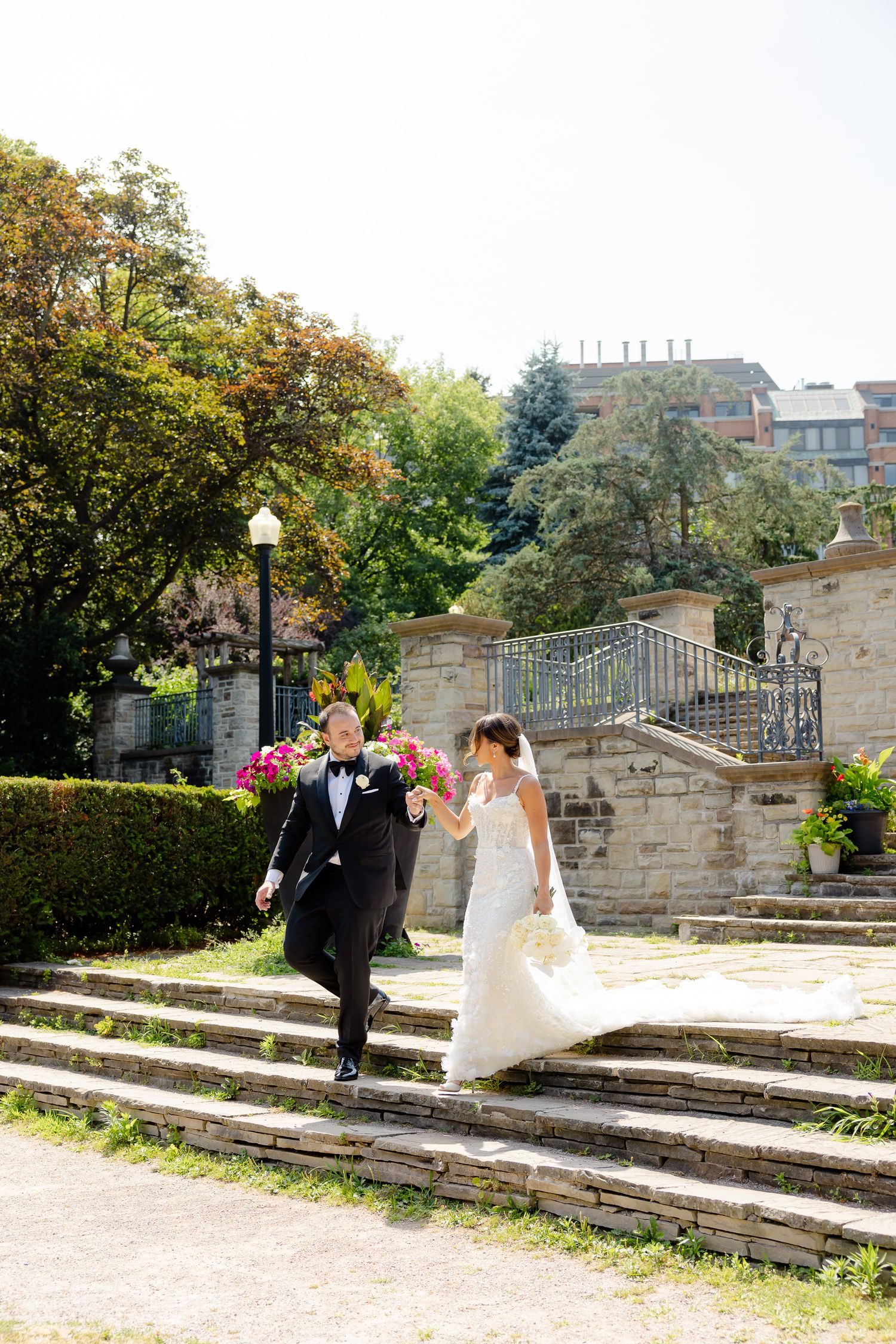 Newlyweds pose together on stone steps in a scenic garden setting during their outdoor fall wedding celebration.
