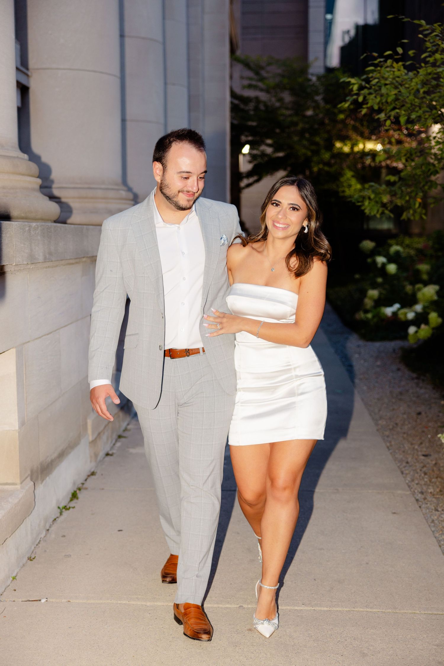Couple walking and smiling together along stone building pathway.